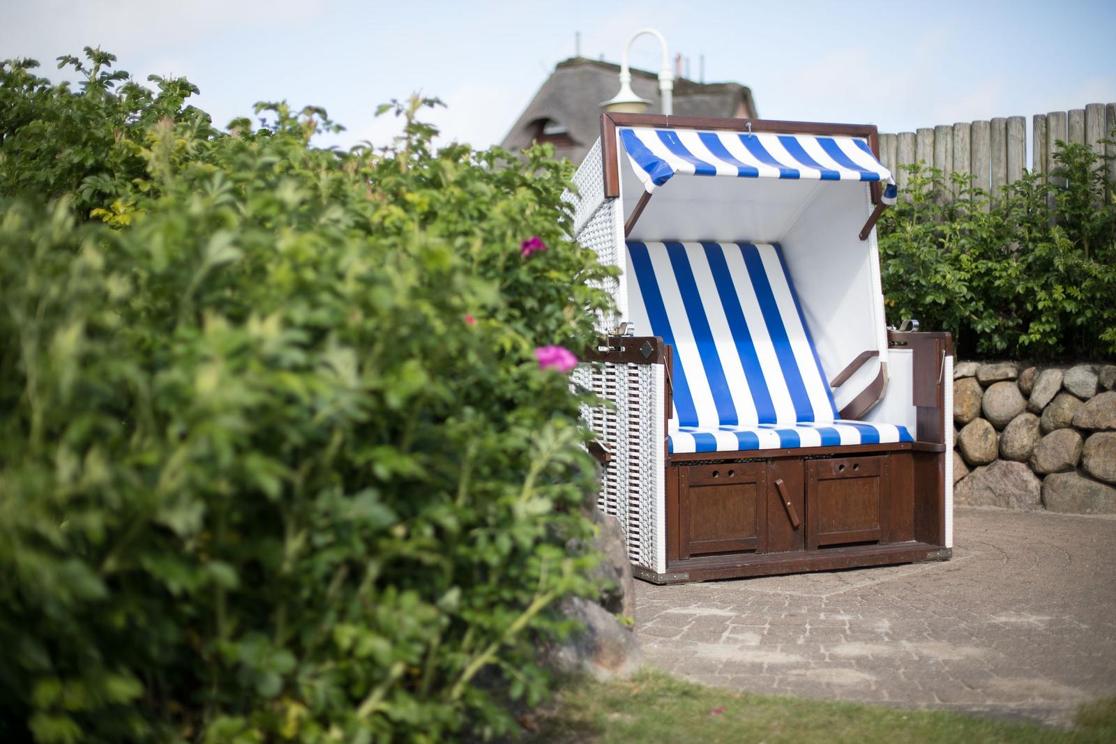 A blue and white beach chair stands in the garden beside shrubs.