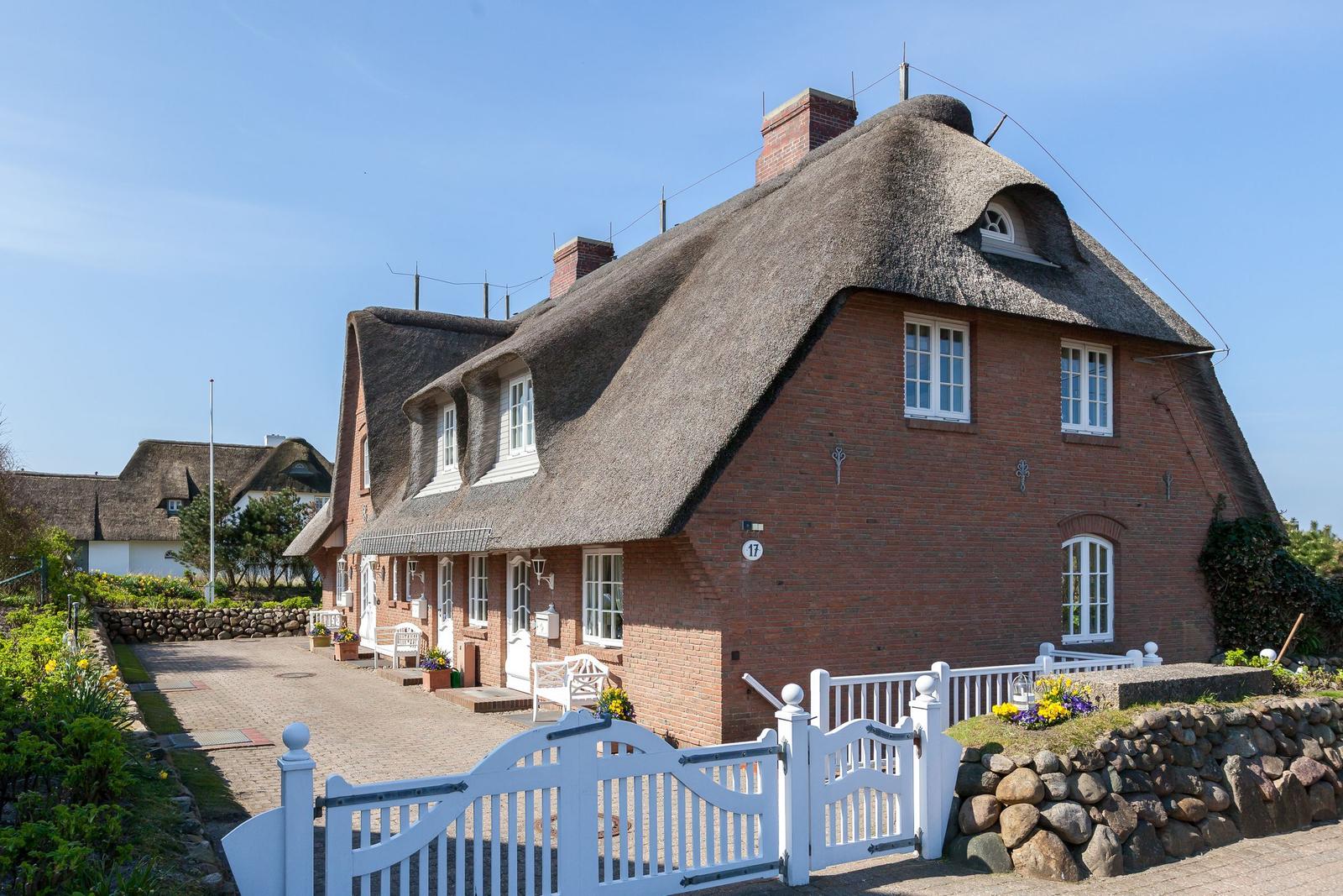 Red brick building with thatched roof and white gate.