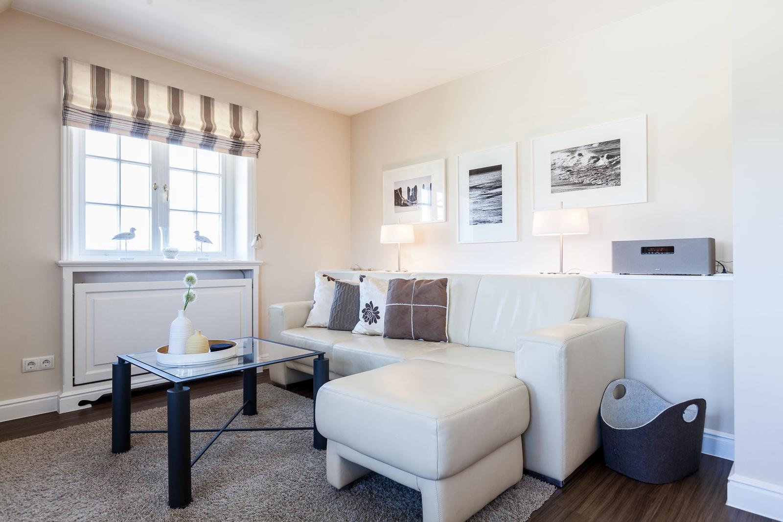 Living room with white sofa, glass table, and window with roller blind.