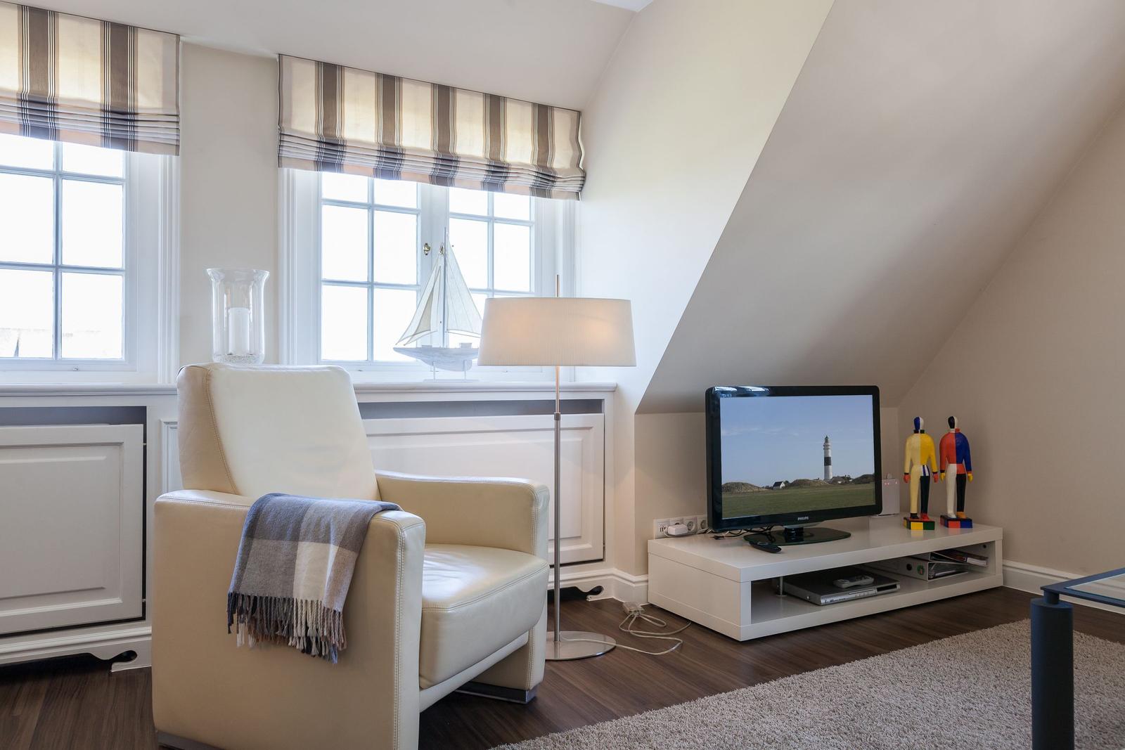 A living room with a chair, TV, and windows under a sloped ceiling.