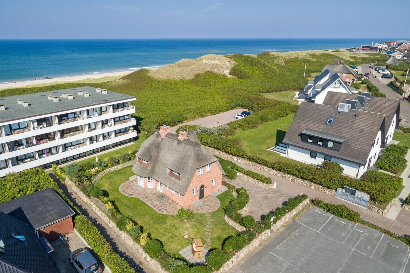Haus mit Strohdach, Grünanlagen und Blick aufs Meer.