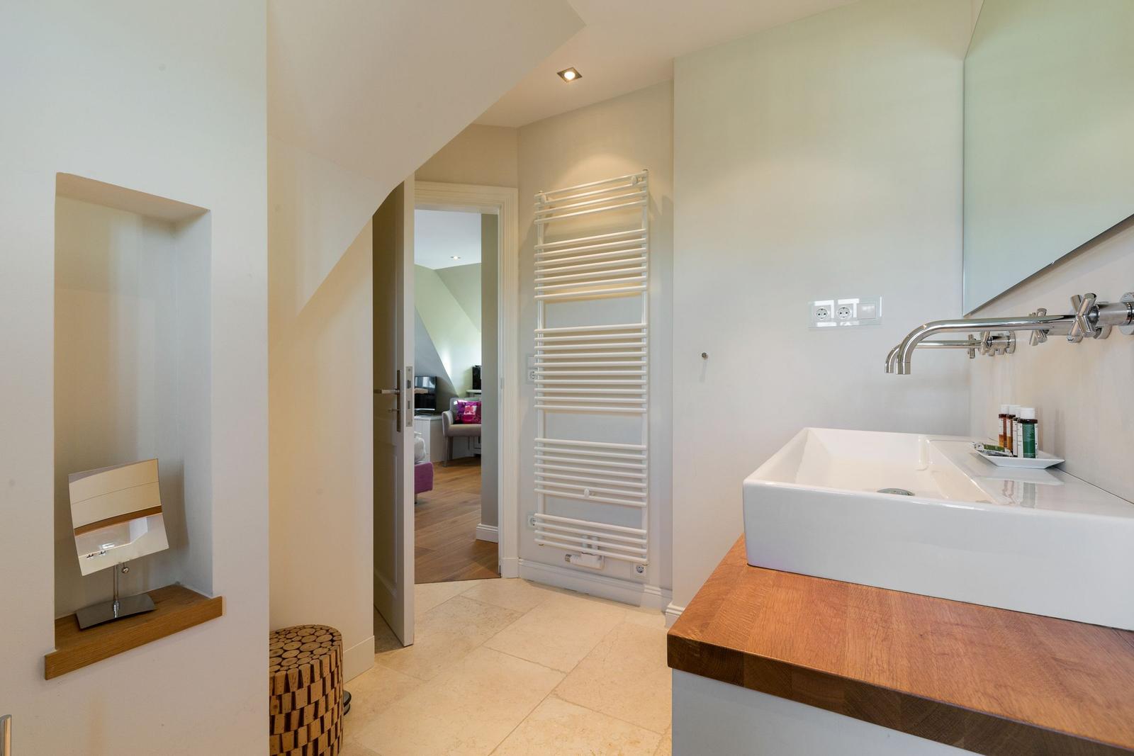 Badezimmer mit Waschbecken, Spiegel und Heizkörper. Tür führt in Wohnbereich.