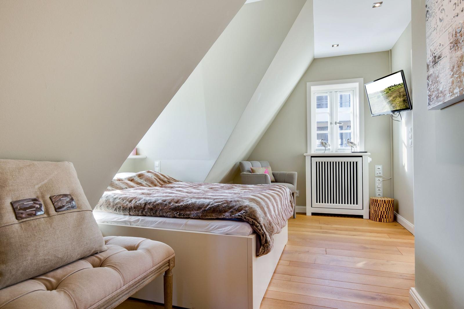 Schlafzimmer mit Dachschrägen, Bett, Sessel und Fenster.