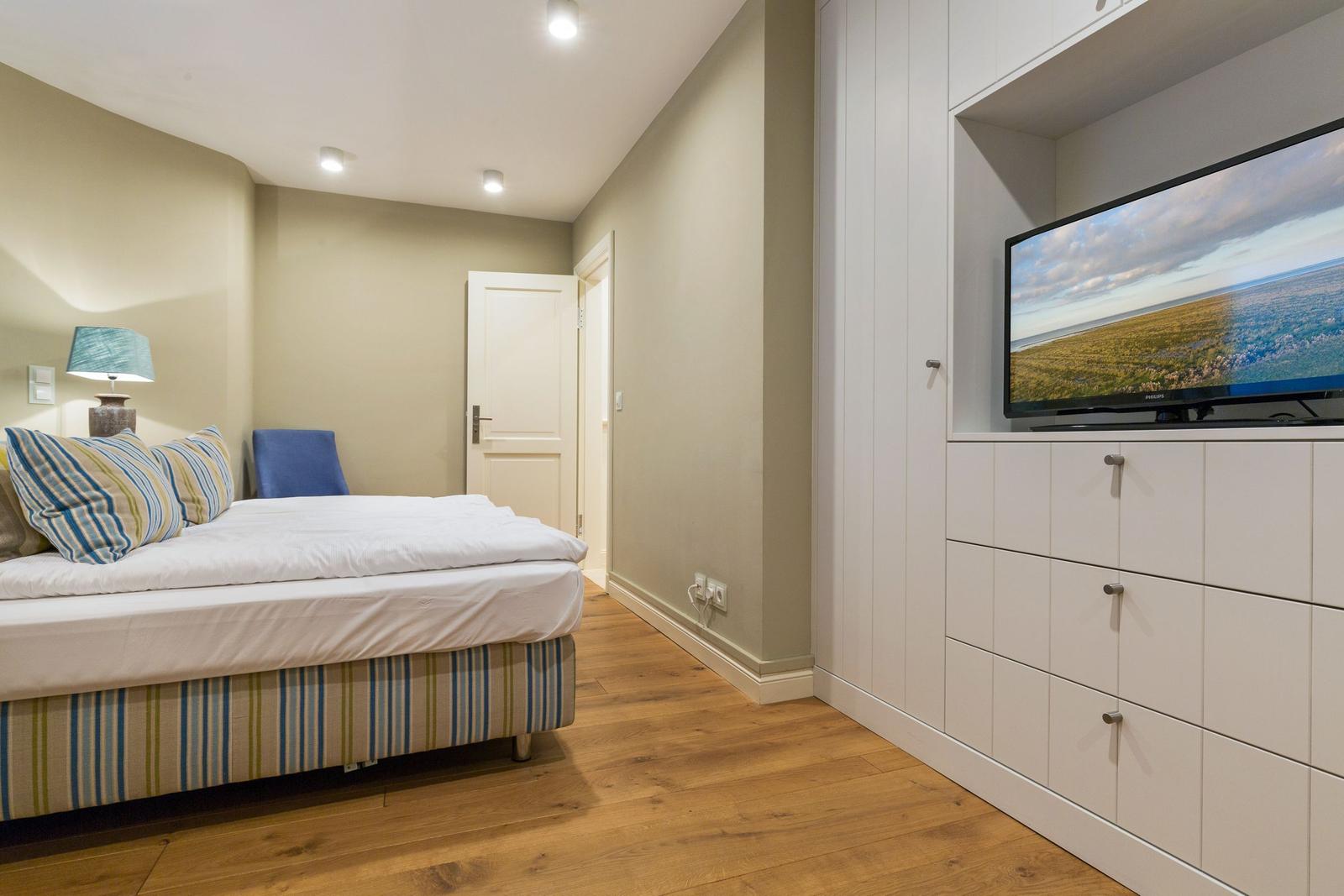 Schlafzimmer mit Bett, Fernseher und Holzboden.