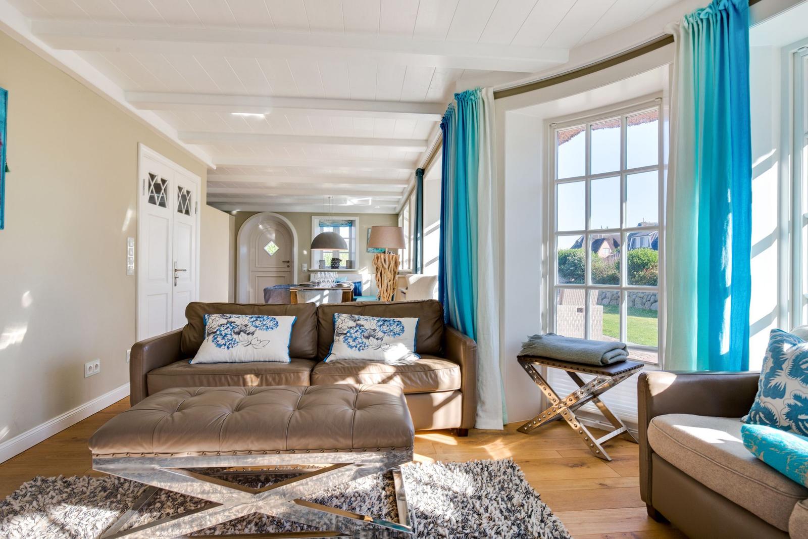 Wohnzimmer mit Sofa, Sitzbank und großem Fenster. Holzboden und blaue Vorhänge.