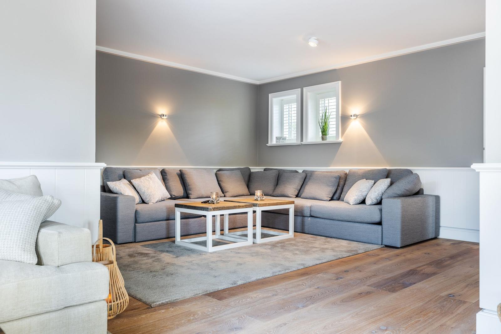 A living room with gray sofa, wooden floor, and two windows on the wall.