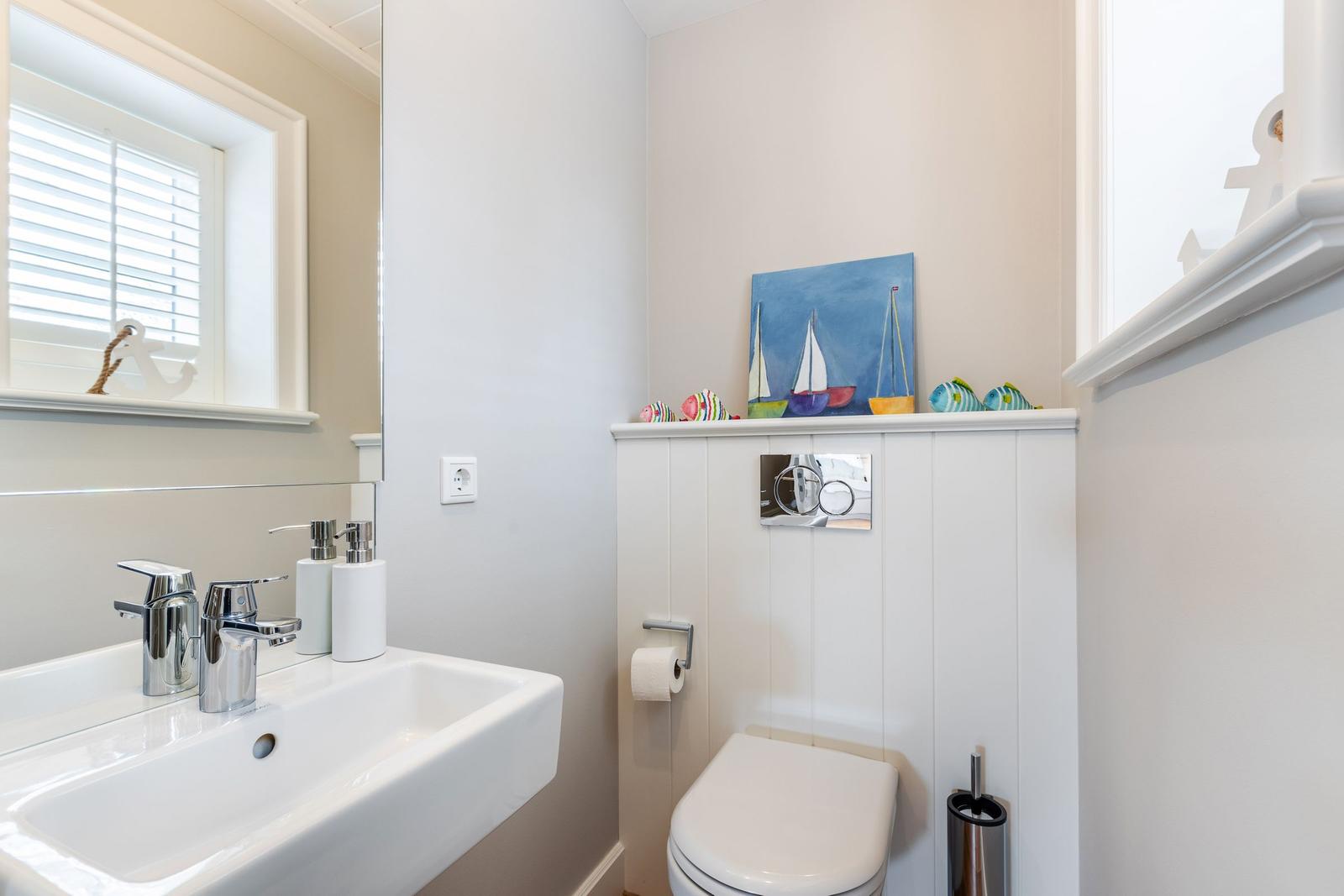 Bathroom with sink, mirror, and toilet. Wall art with sailboats and decorative fish.