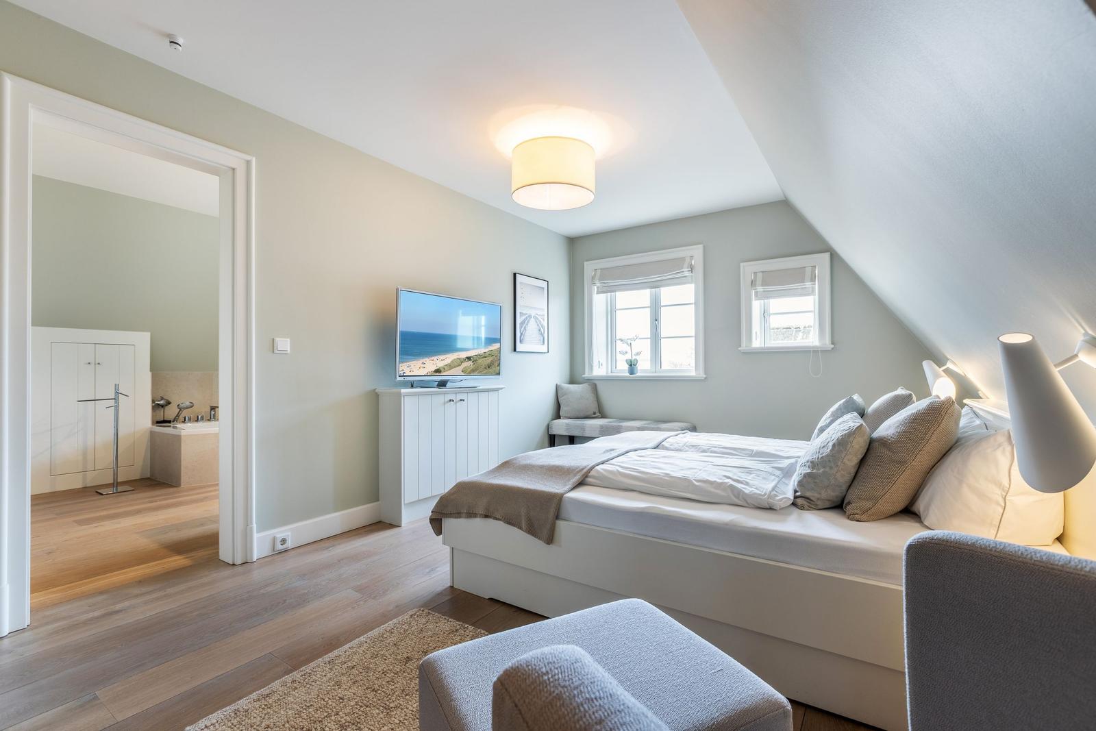 Bedroom with sloped ceiling, bed, TV, and view into bathroom