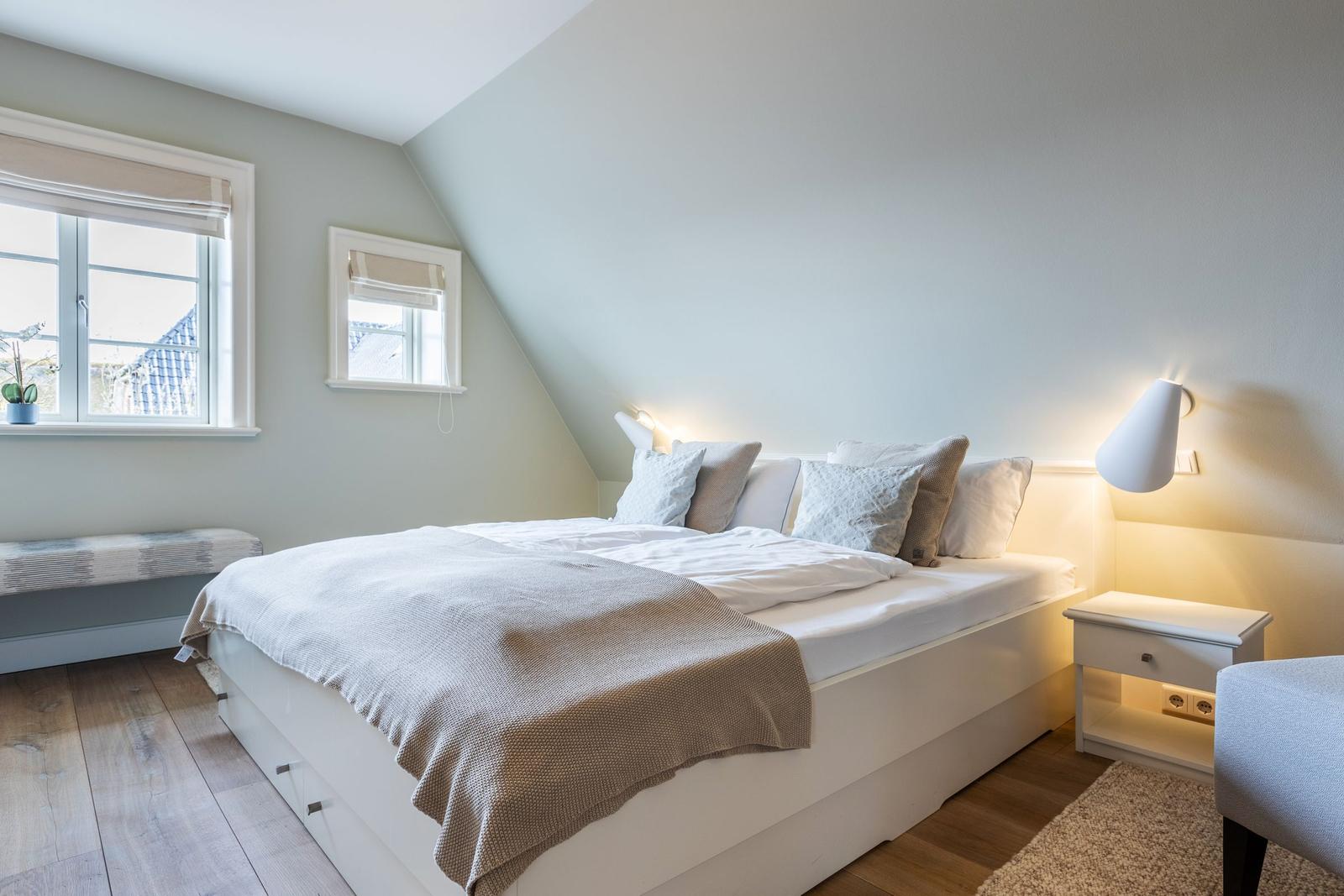 Bedroom with sloped ceiling, bed, nightstand, and windows.