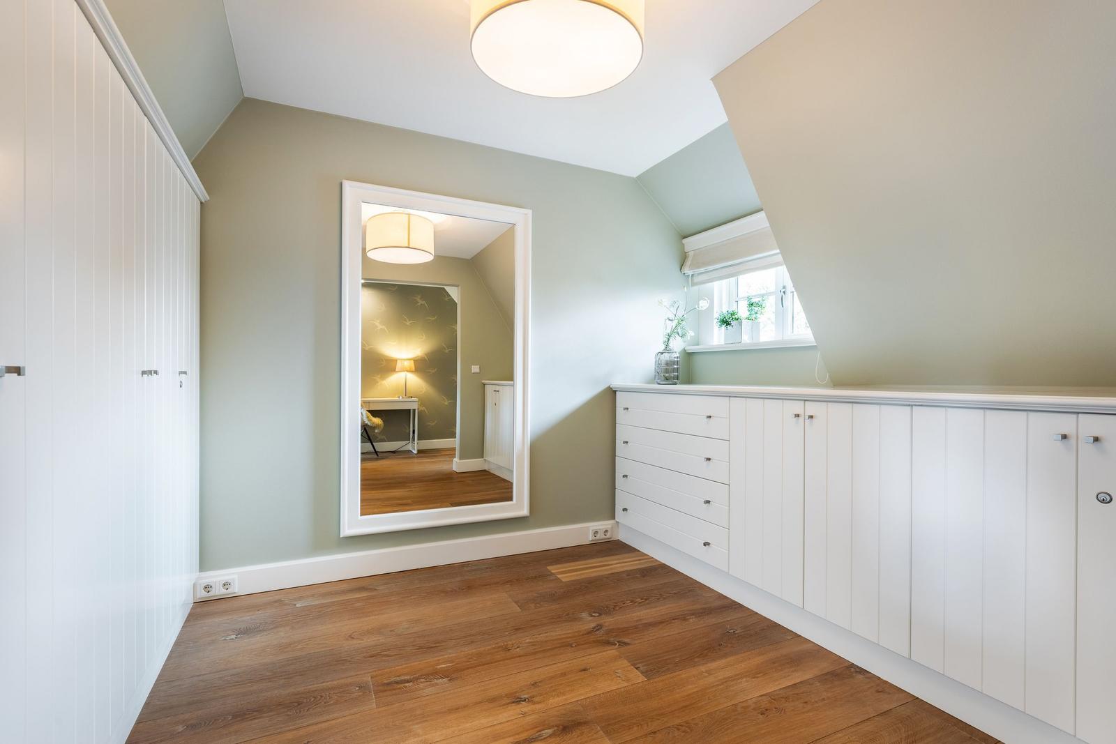 Bedroom with wooden floor, white closet, and mirror. Window with roller blind.