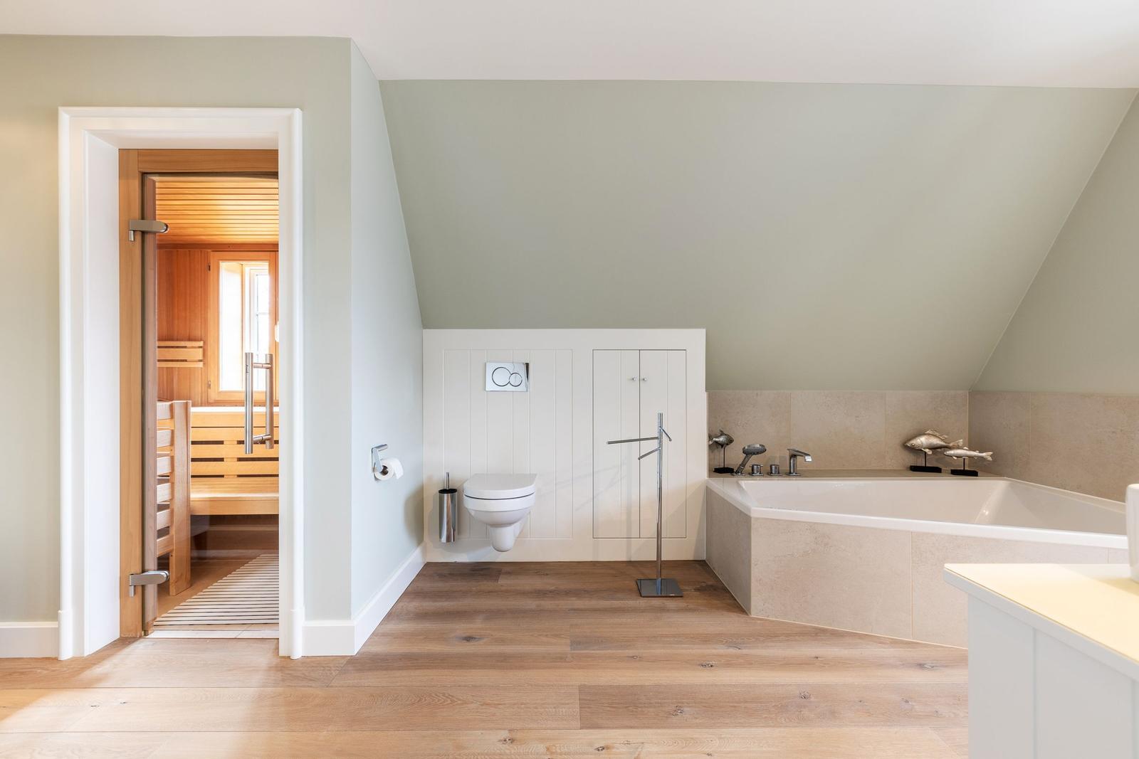 Bathroom with bathtub, toilet, and sauna. Wooden floor and light gray walls.