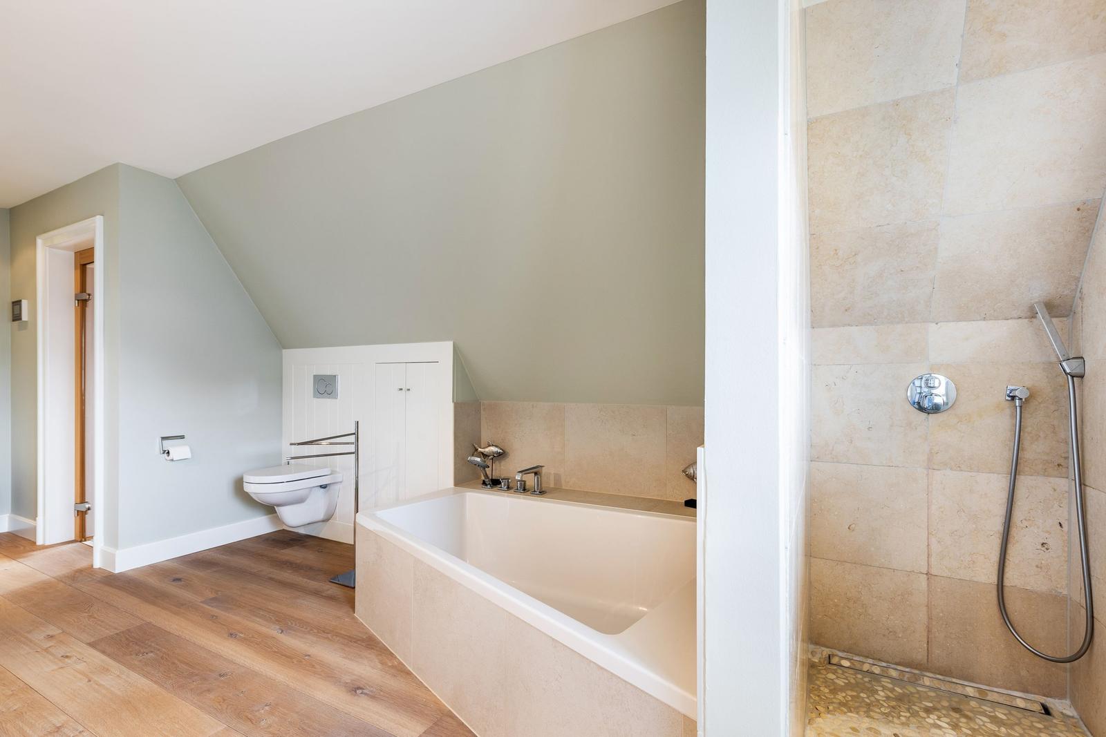 Bathroom with bathtub, shower, and toilet under sloped ceiling