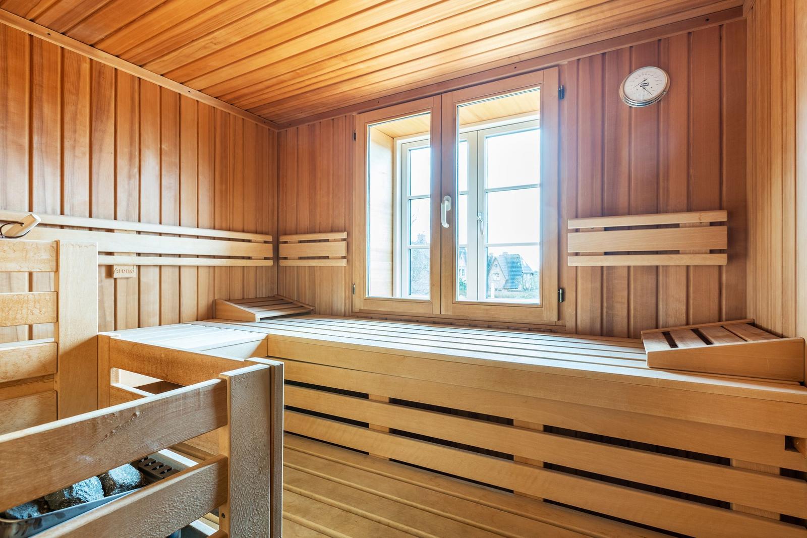 Sauna with wooden bench, window, and thermometer on the wall.