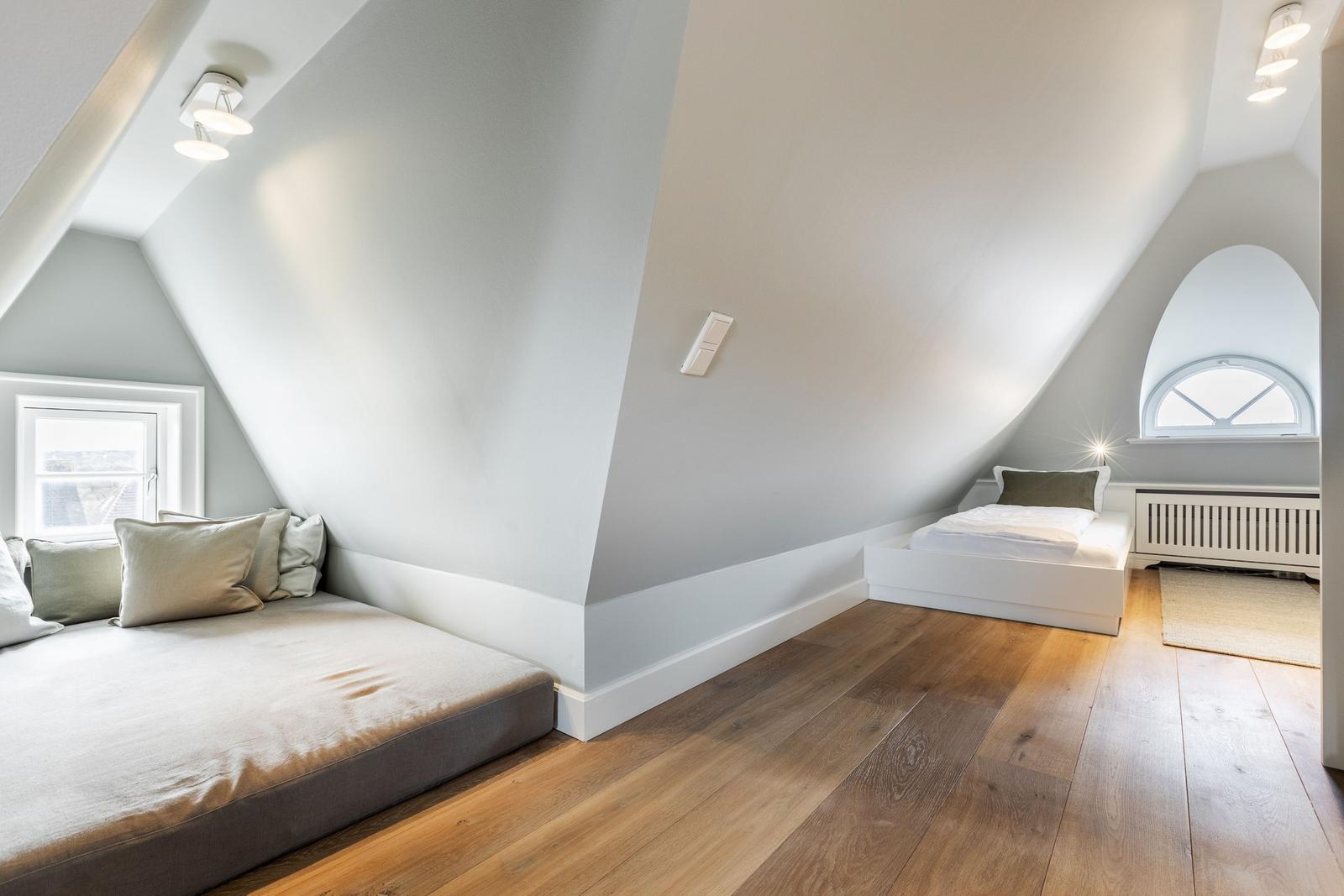 Room with sloped ceilings, two beds, and hardwood floor.