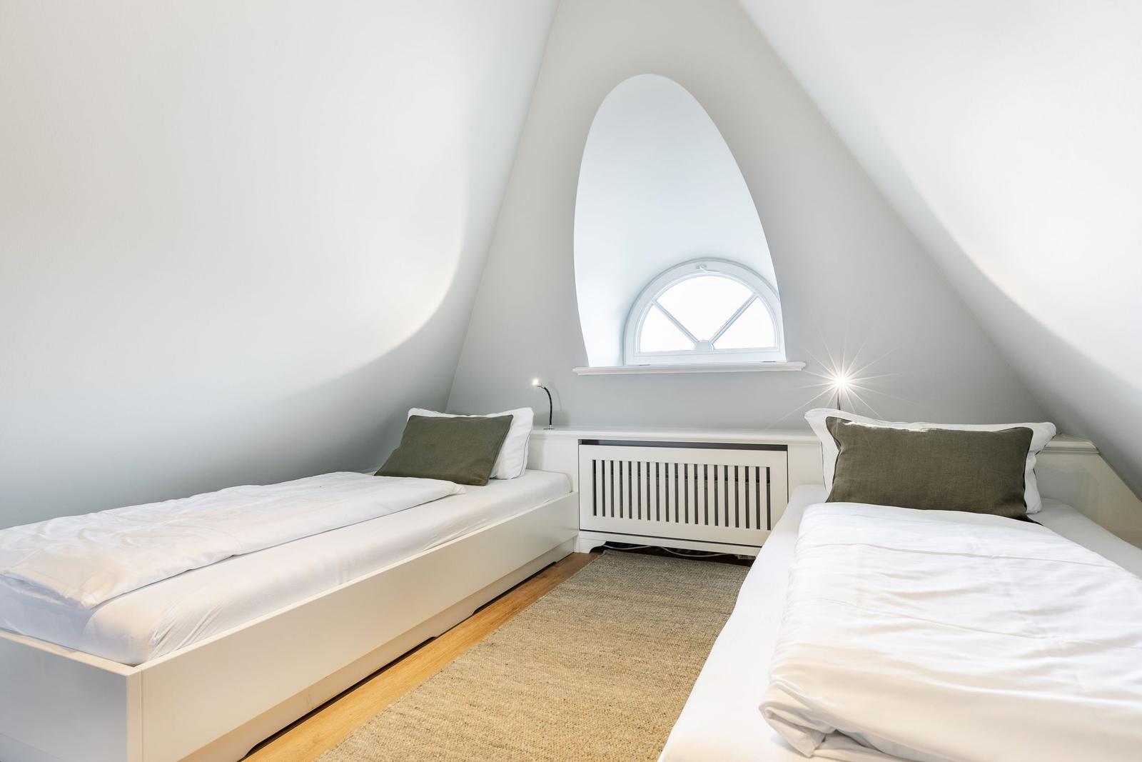 Two single beds under sloped ceilings with window and radiator.