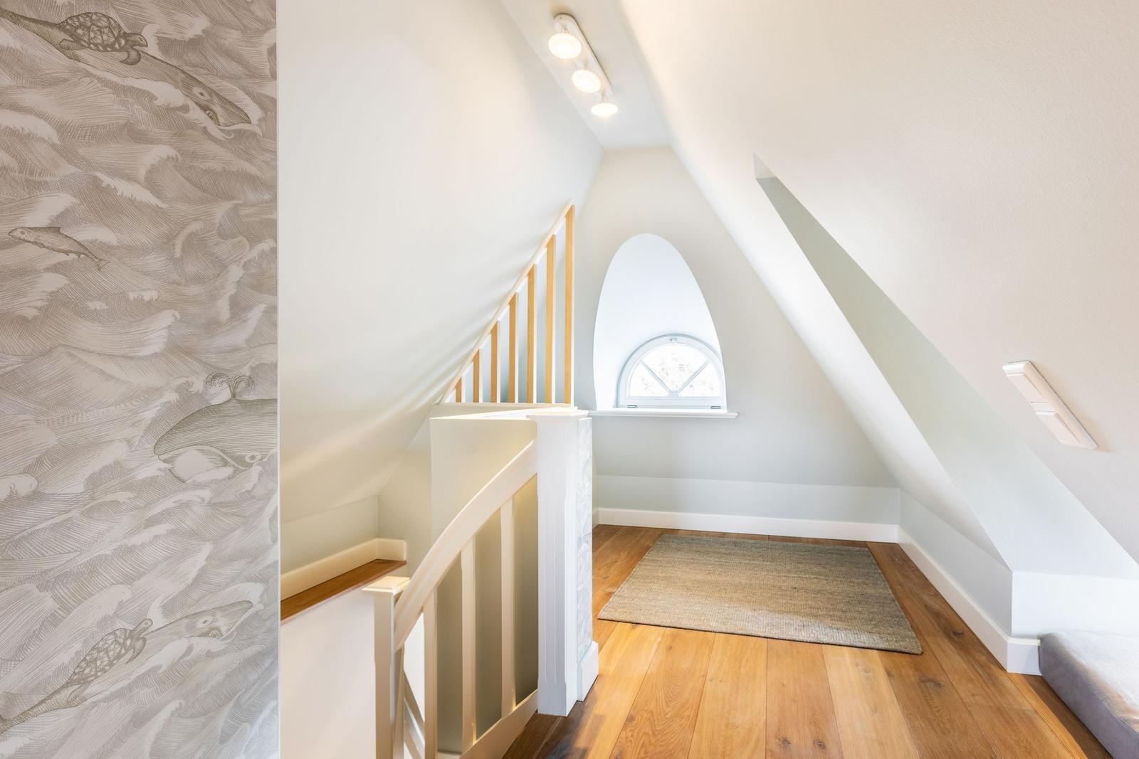 Staircase with wooden floor, arched window, and wallpaper with sea creature motifs.