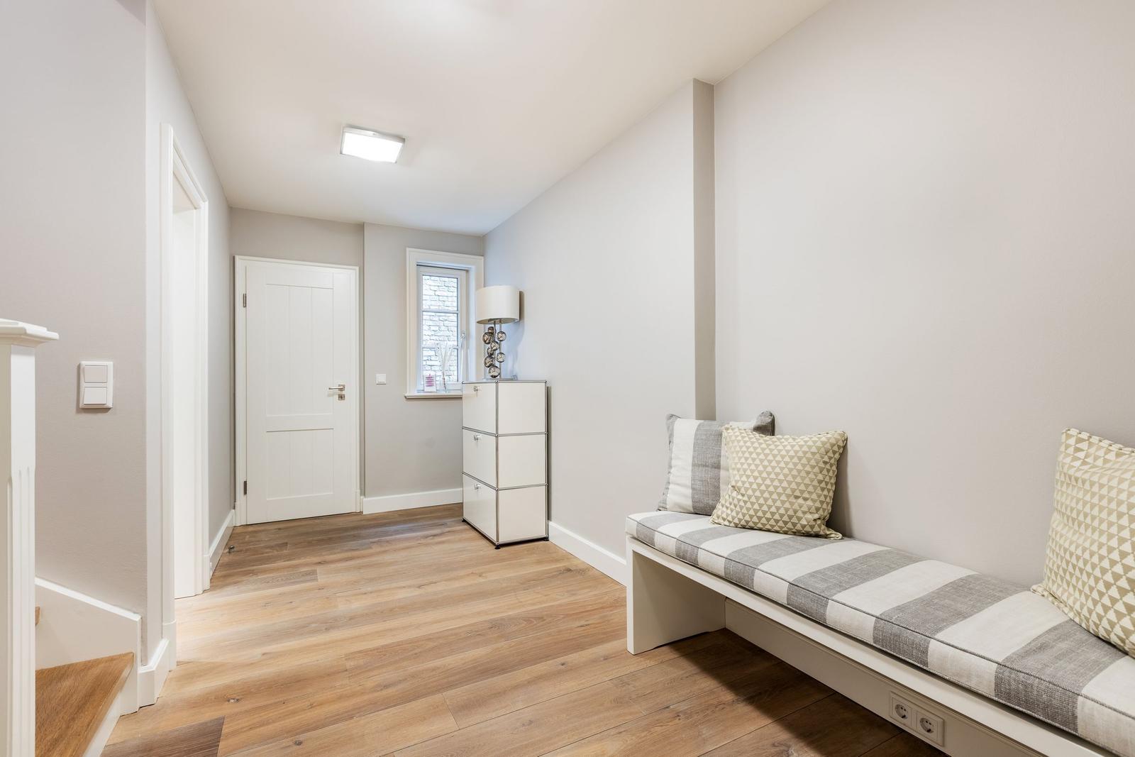 Hallway with bench, cabinet, and window. Wooden floor and white walls.