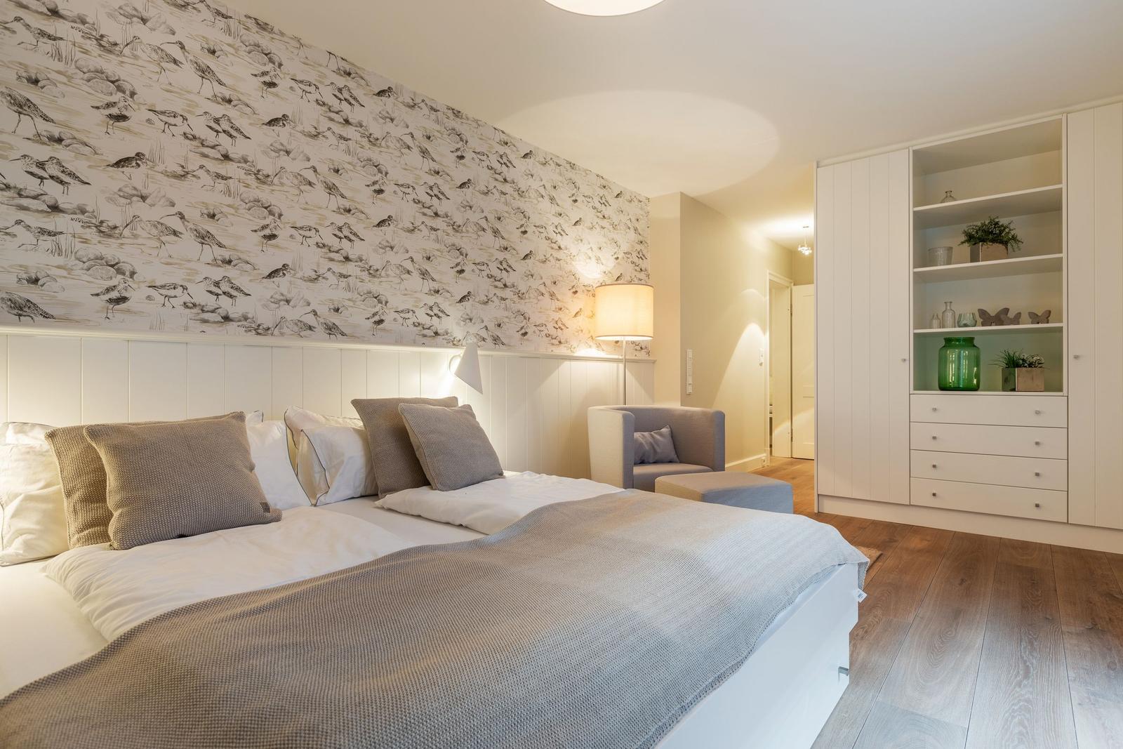 Bedroom with bed, bird-patterned wallpaper, and white wardrobe.