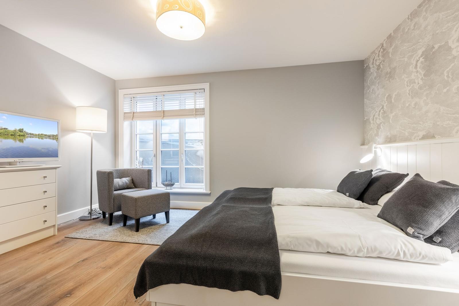 Bedroom with bed, window, TV, and seating area.