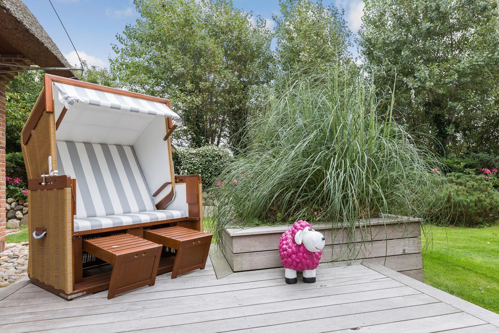 Deck with beach chair and pink sheep sculpture in front of greenery