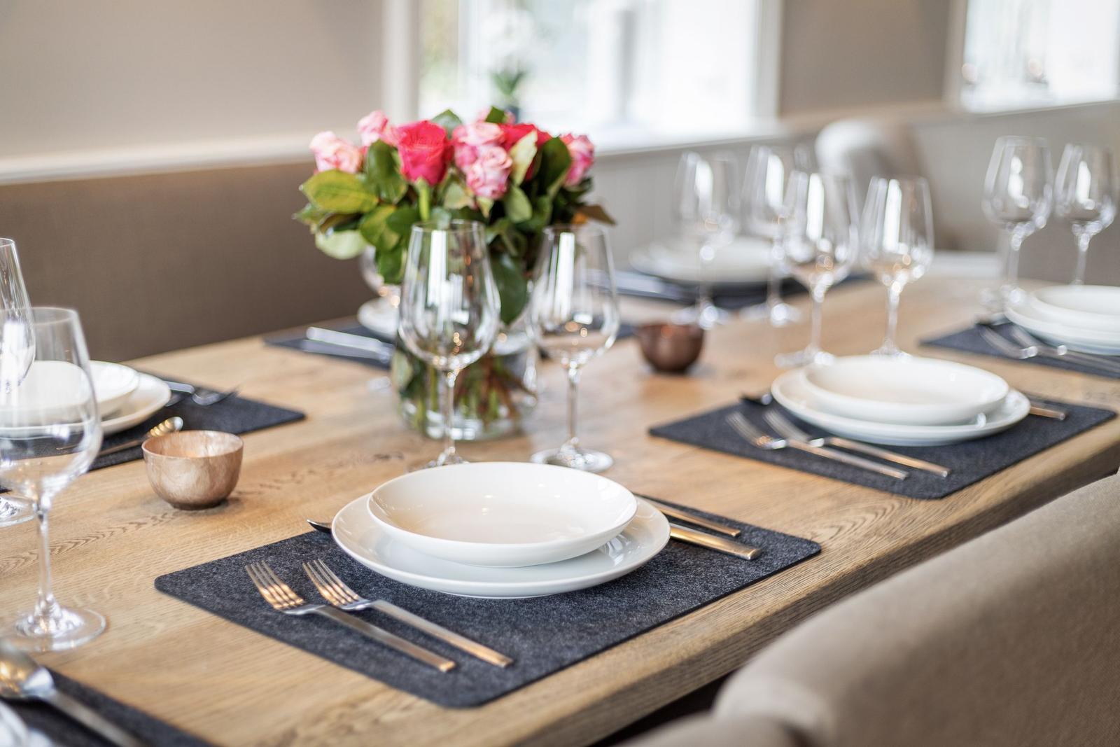 Dining table with placemats, plates, and glasses. A vase with flowers is in the center.