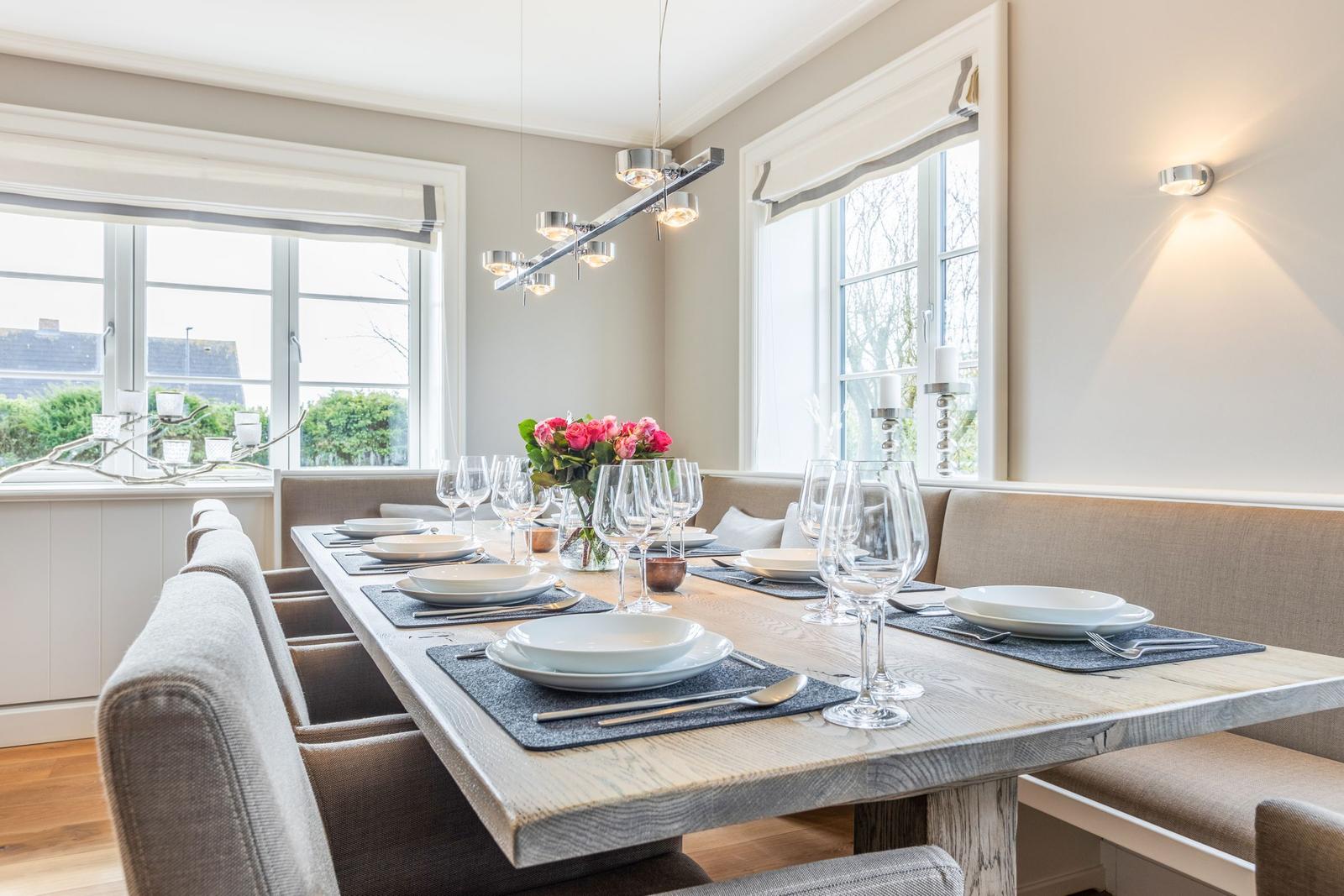 Dining room with long table, chairs, and windows. Table set with dishes and flowers.