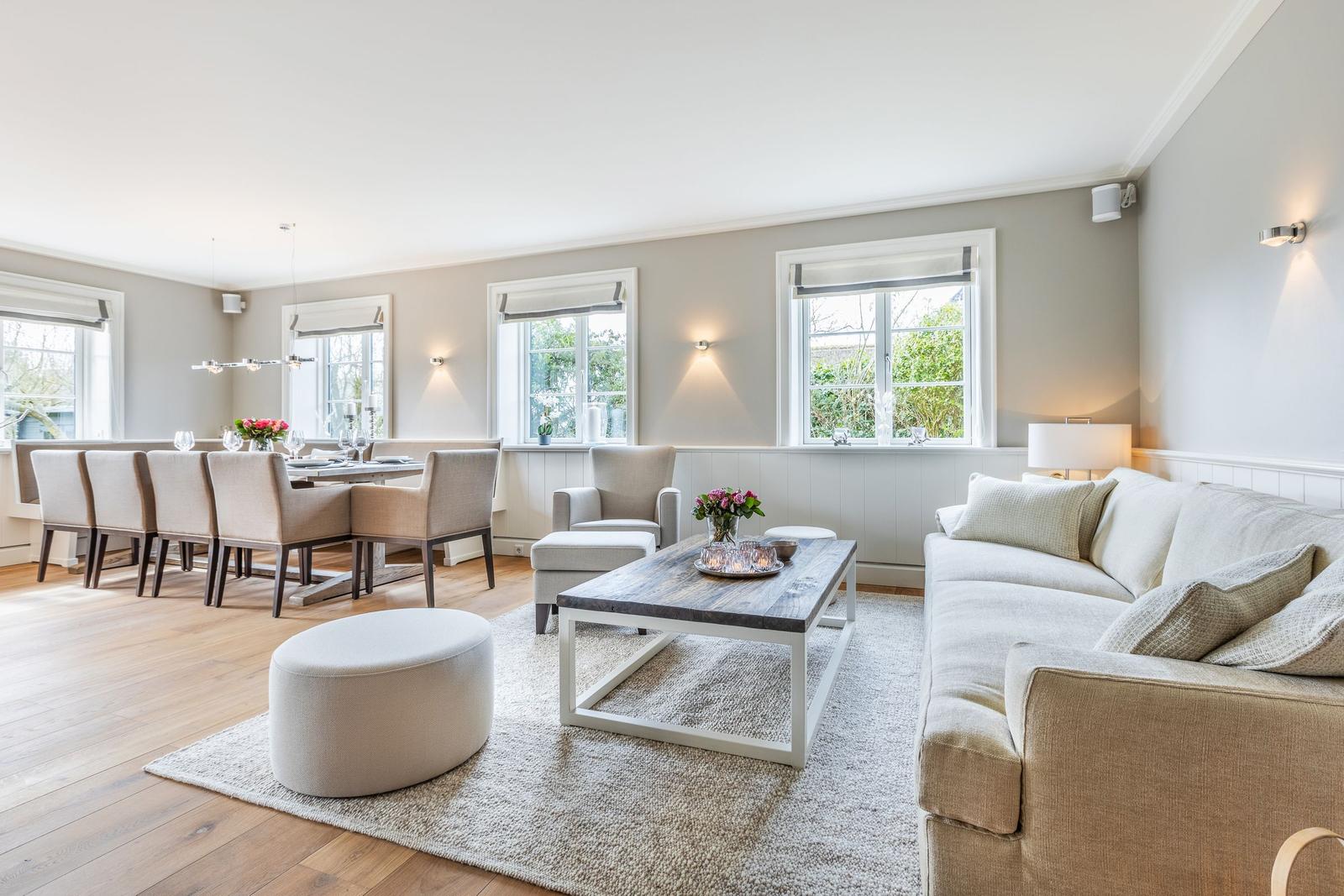Living and dining area with sofa, table and chairs. Wooden floor and windows with view outside.