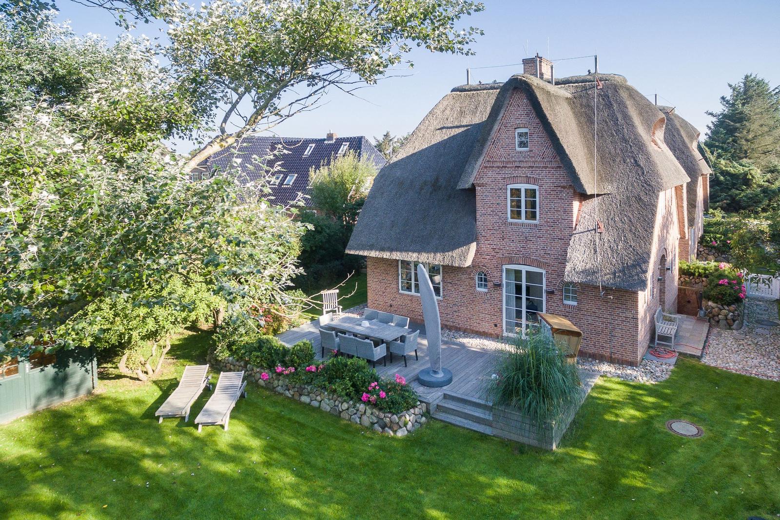 Red brick house with thatched roof, garden with sun loungers and terrace.