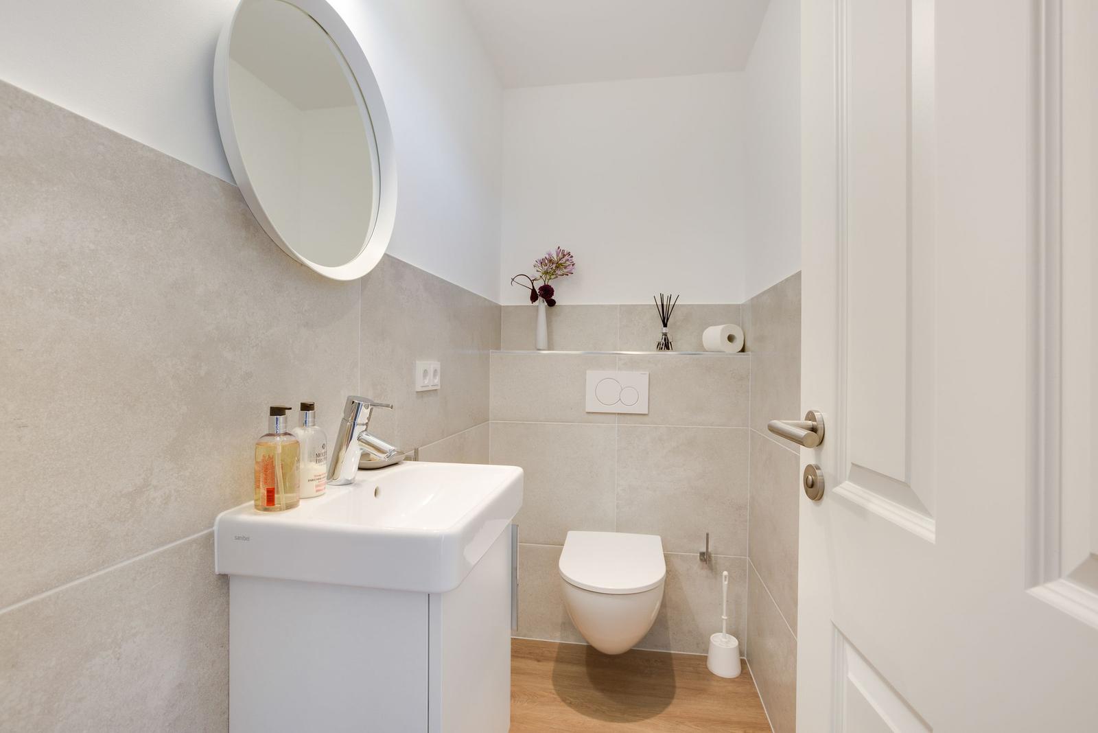 Badezimmer mit Waschbecken, Toilette und runden Spiegel an der Wand.