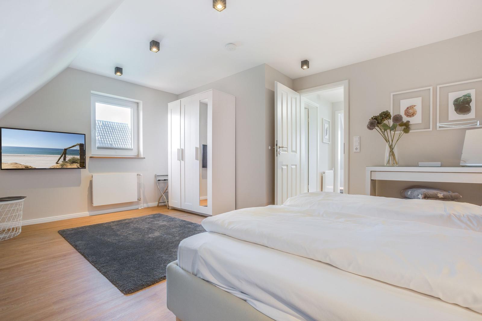 Schlafzimmer mit Doppelbett, Schrank und Fenster. Wandbild und Teppich sichtbar.