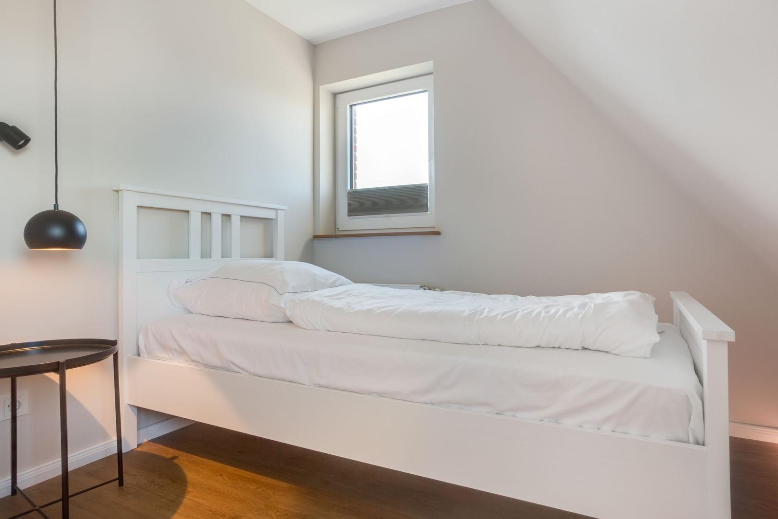 Ein Schlafzimmer mit weißem Bett, Fenster und schwarzem Hängelampen.