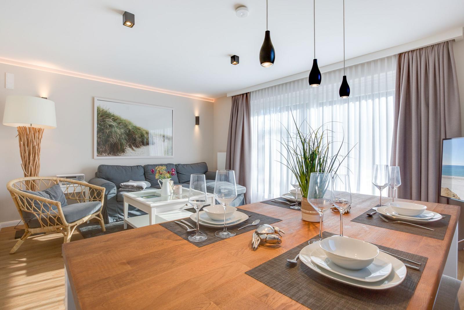 Esszimmer mit Holztisch, Stühlen und Glastisch. Sofa, Wandbild und Fenster mit Vorhängen.