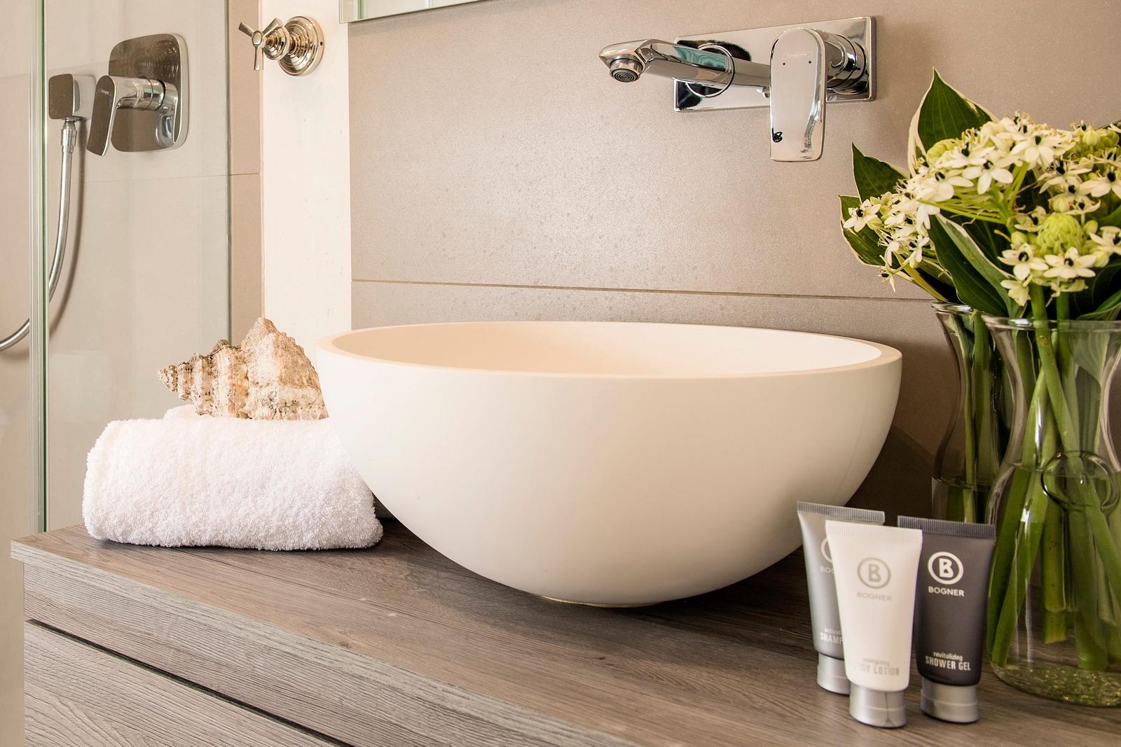 Sink with seashell, towels, and flowers on wooden countertop.