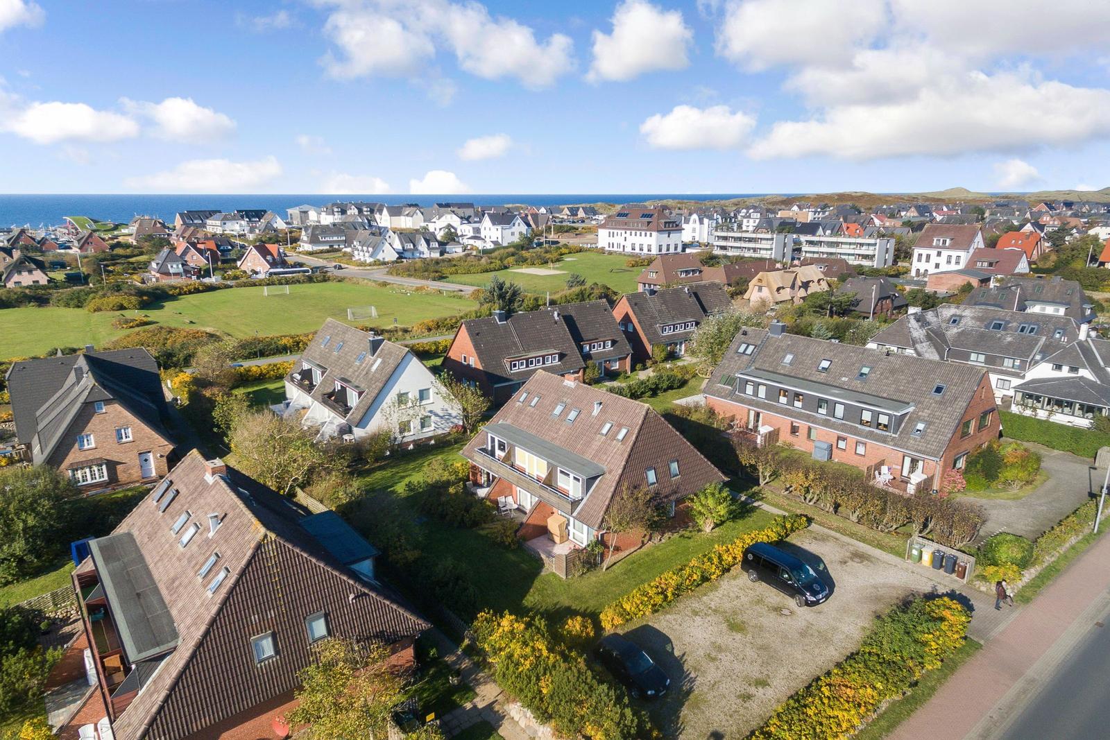 Village with houses and green areas by the sea under blue sky.