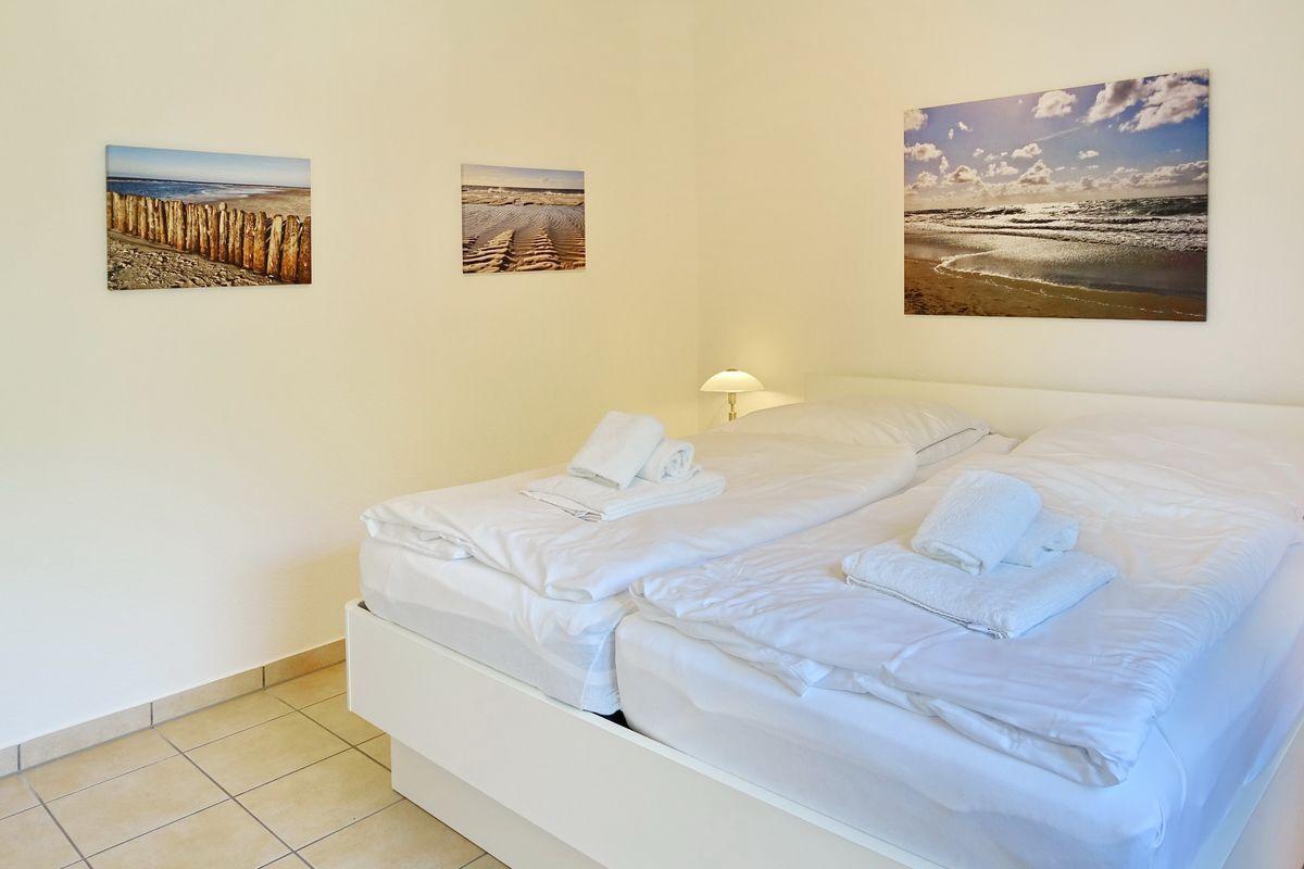 Room with double bed, white linens, and beach pictures on the walls.