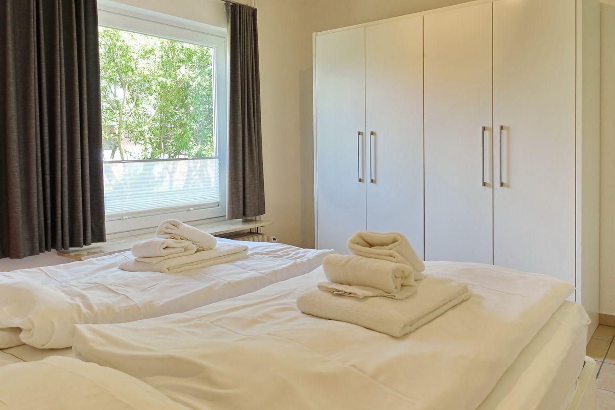 Two beds with white bedding and folded towels. Trees are visible outside the window.