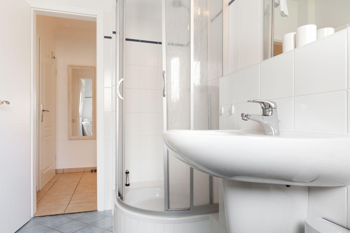 Bathroom with shower, sink, and mirror. Corridor leads to a room with mirror.