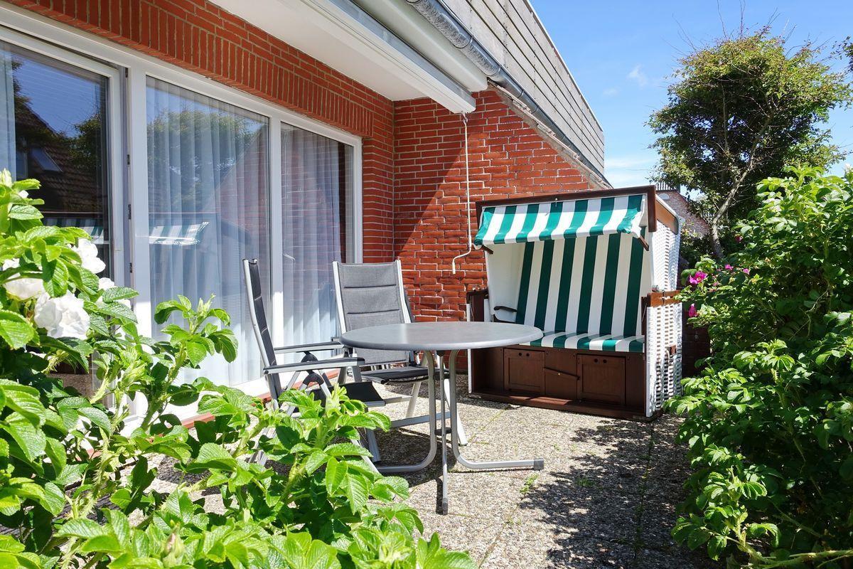 Terrace with lounge chair, table, and beach chair beside red brick house.