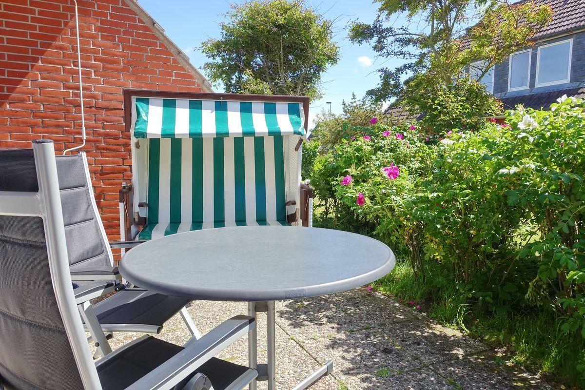 Terrace with table, chairs, and beach chair in front of red brick house.