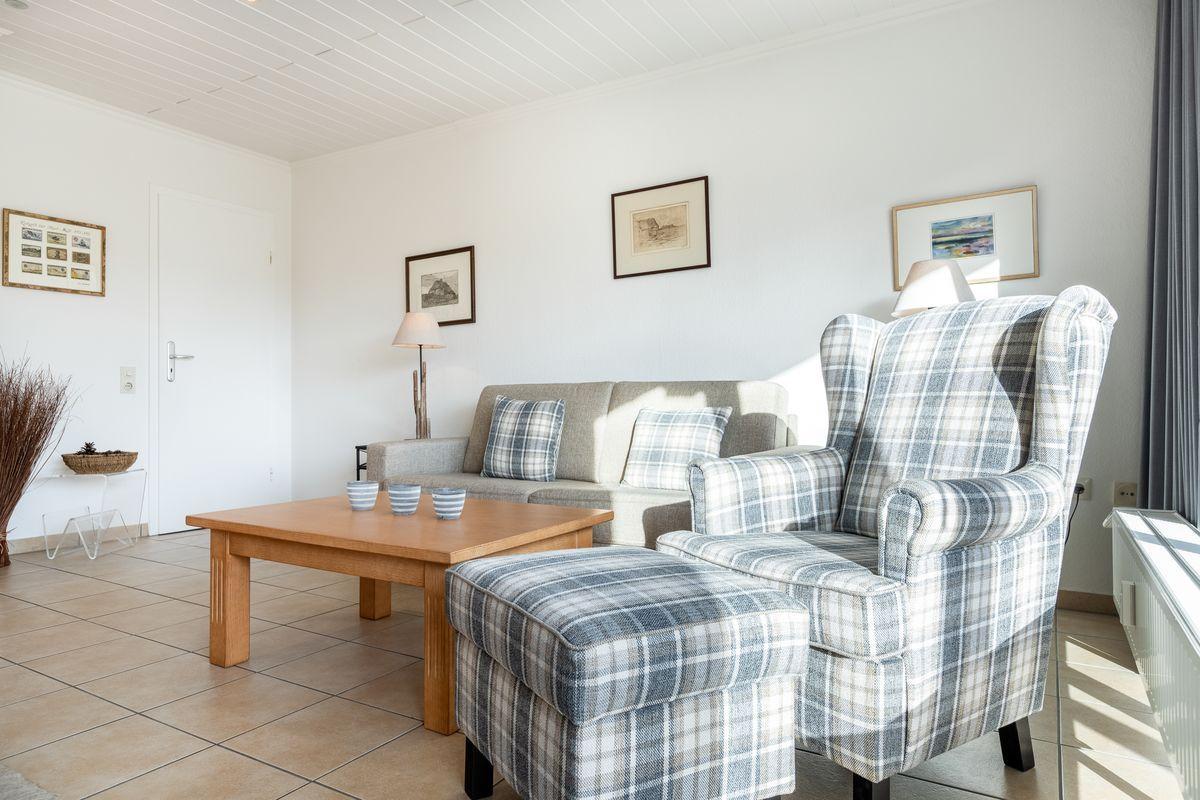 Living room with sofa, armchair, and table. Wall art and window visible.