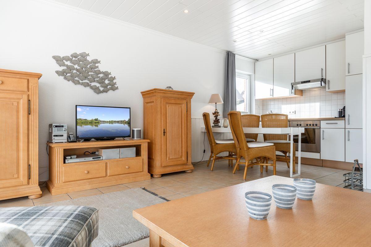 Living room with dining area and kitchen. Wooden furniture, TV, and kitchen visible.