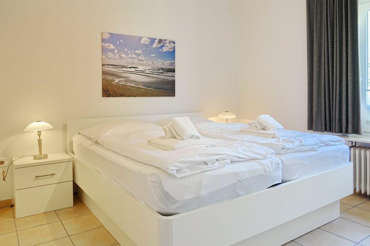 Bedroom with white bed, nightstand, and wall picture.