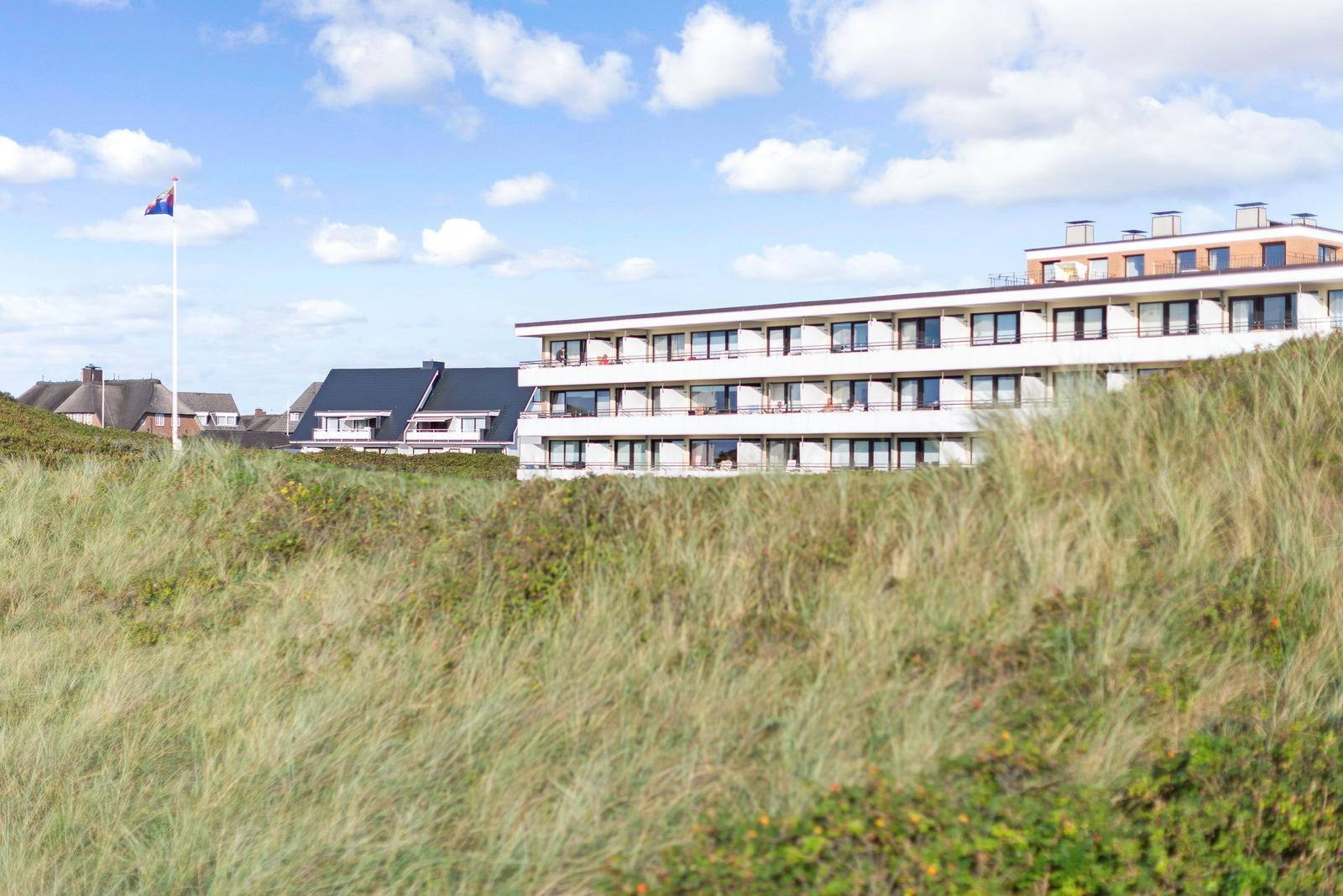 Modern building with balconies behind dunes and flag in background.
