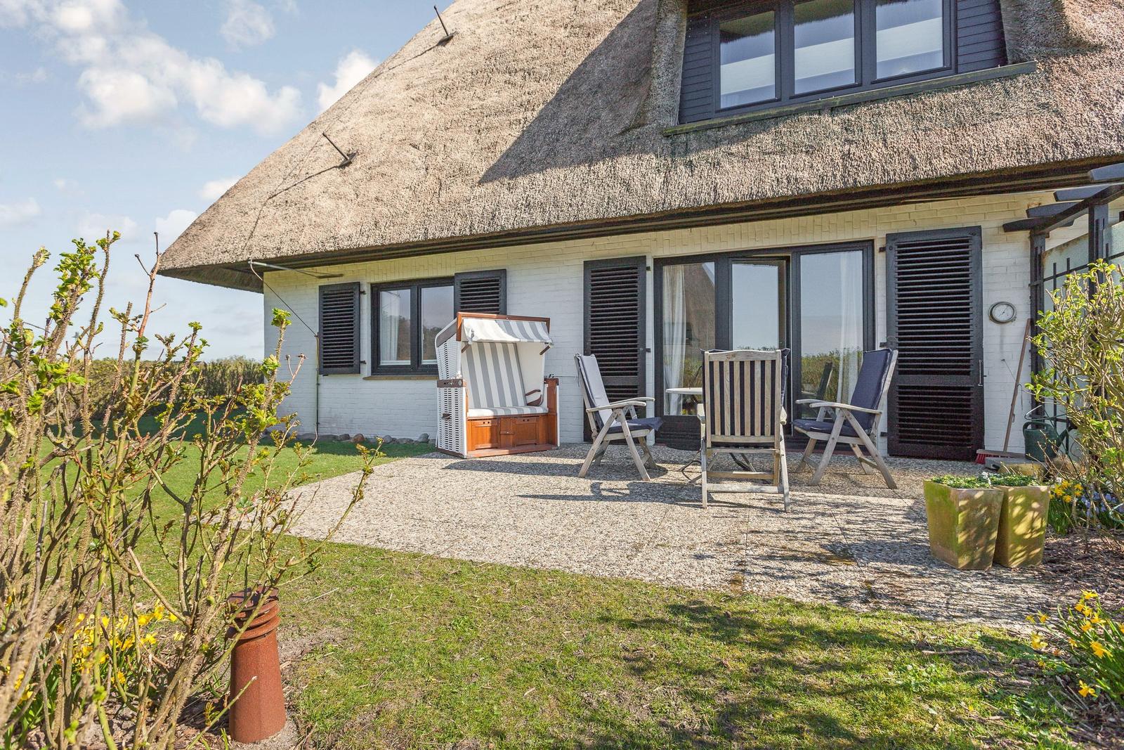 Haus mit Strohdach, Terrasse mit Liegestühlen und Strandkorb.