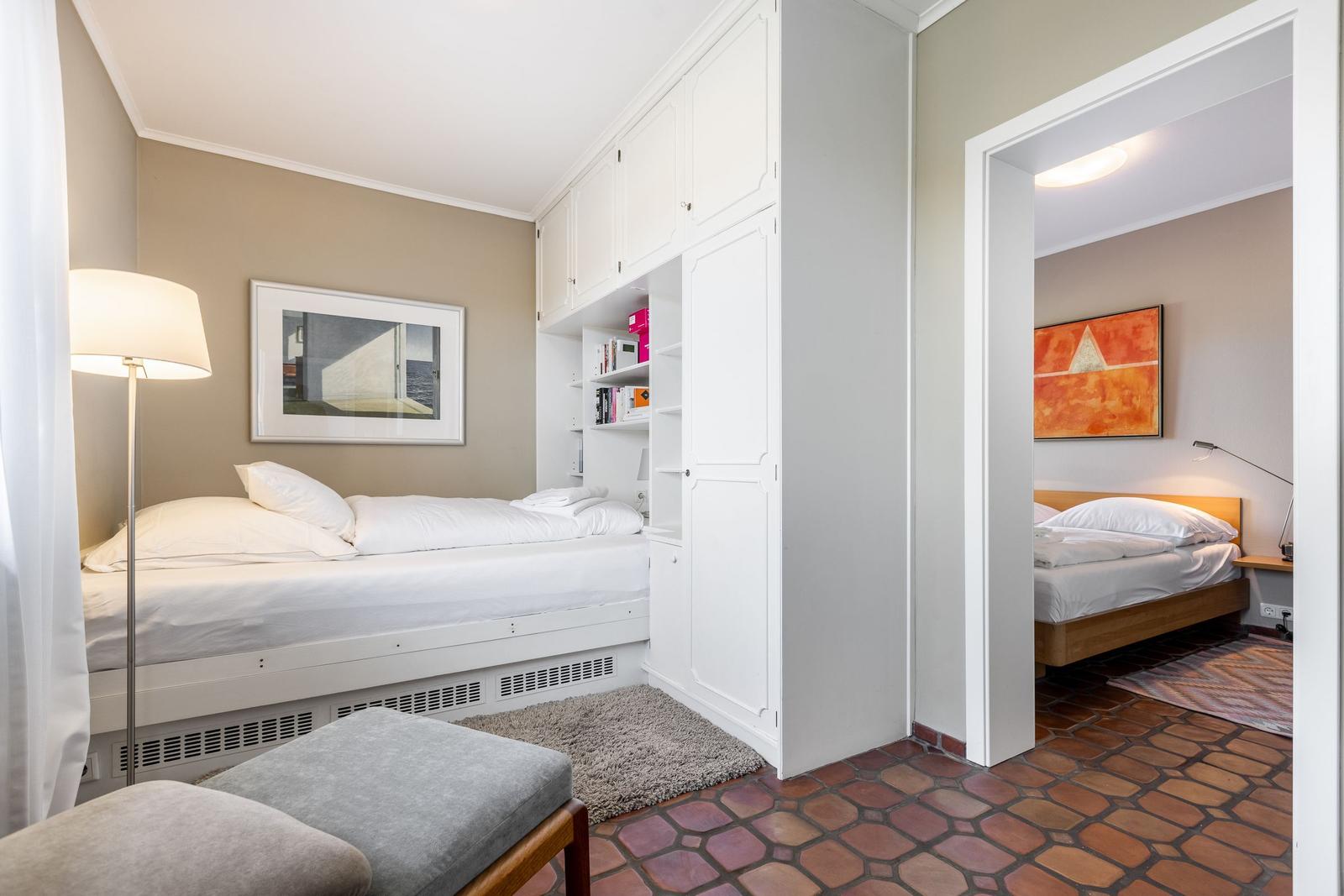 Zimmer mit Bett, Schrank und Bild an der Wand. Durchgang zu einem weiteren Schlafzimmer.