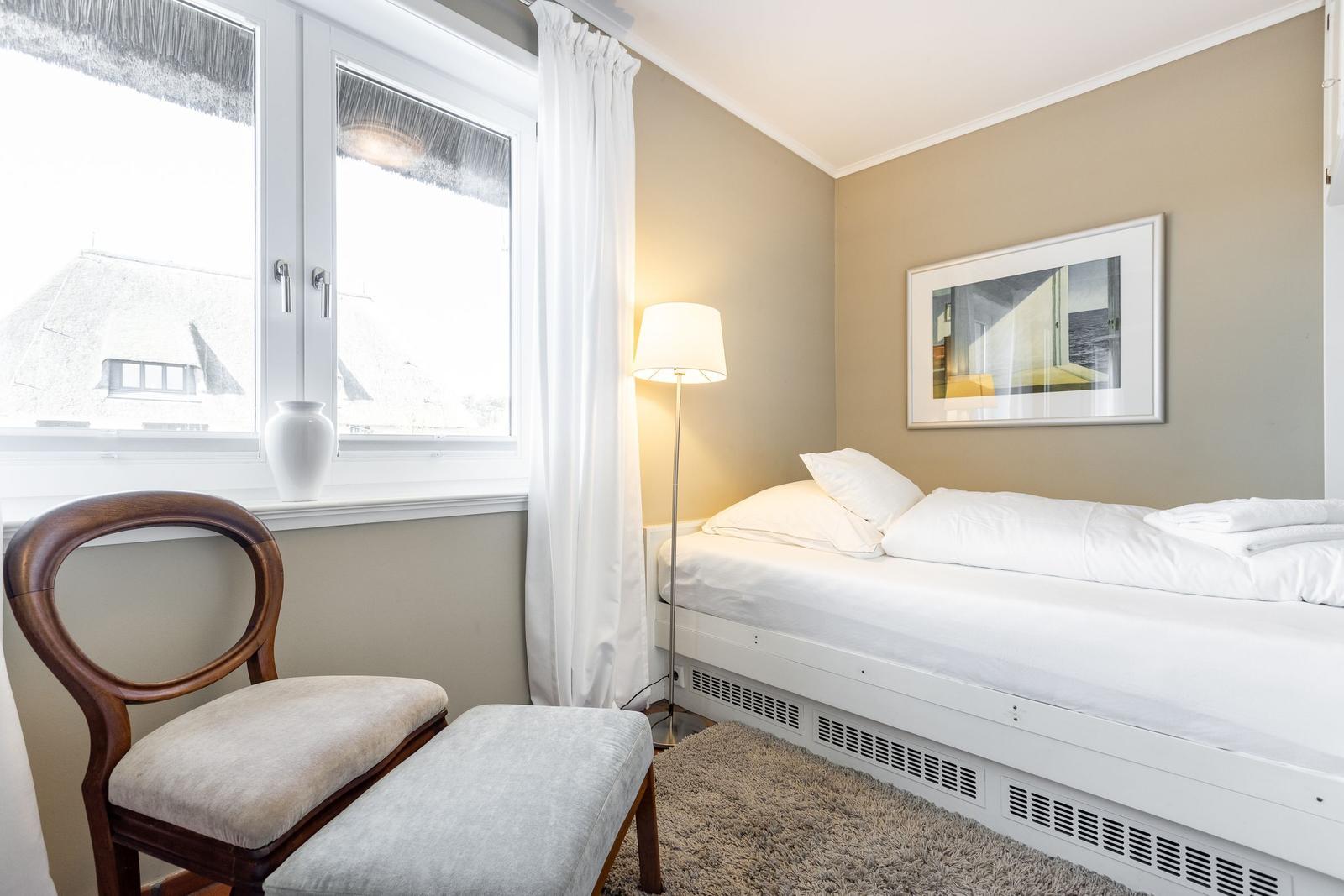 Schlafzimmer mit Bett, Stuhl, Fenster und Wandbild.