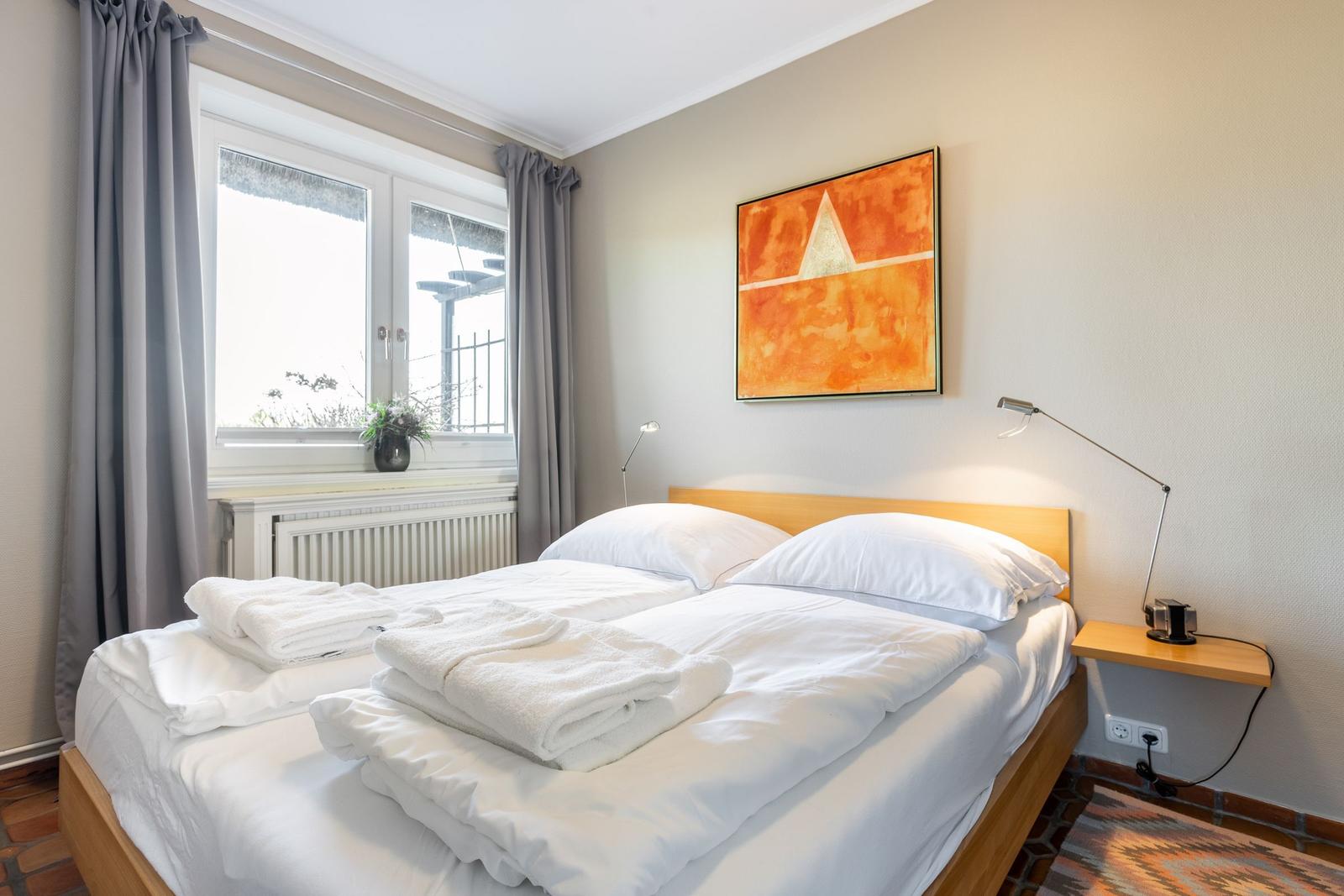 Schlafzimmer mit Bett, Fenster und Wandbild.