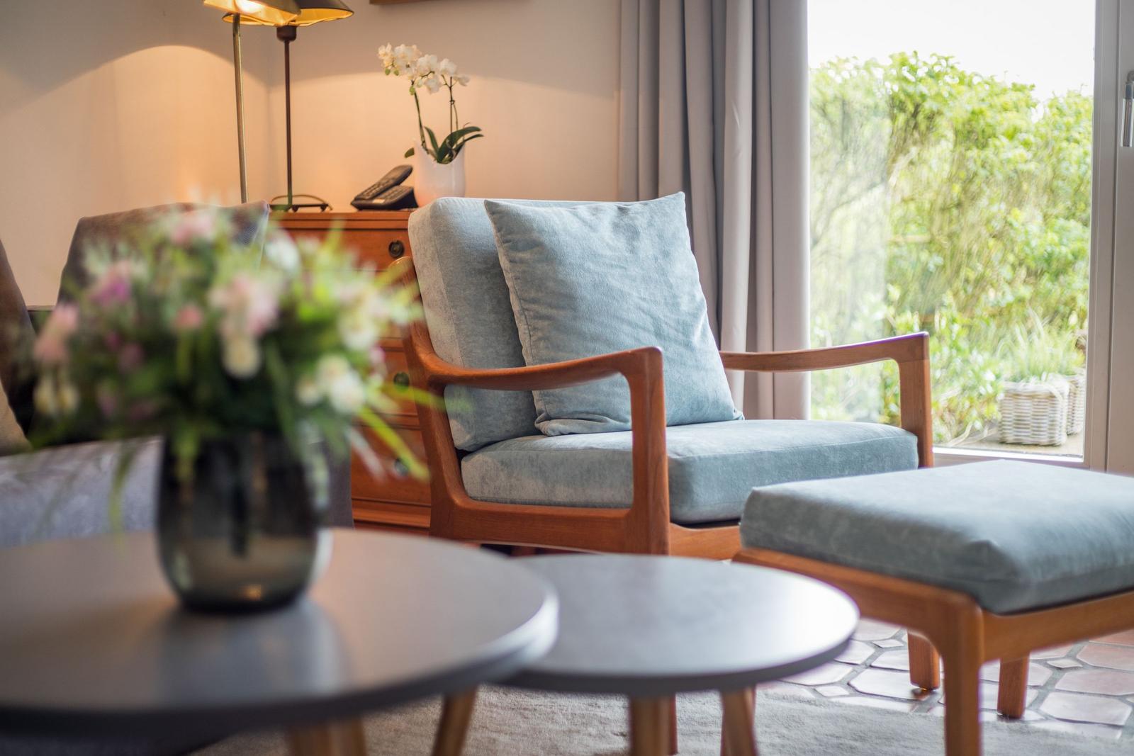 Ein Sessel mit Kissen und Fußhocker vor einem Fenster mit Blick auf einen Garten.