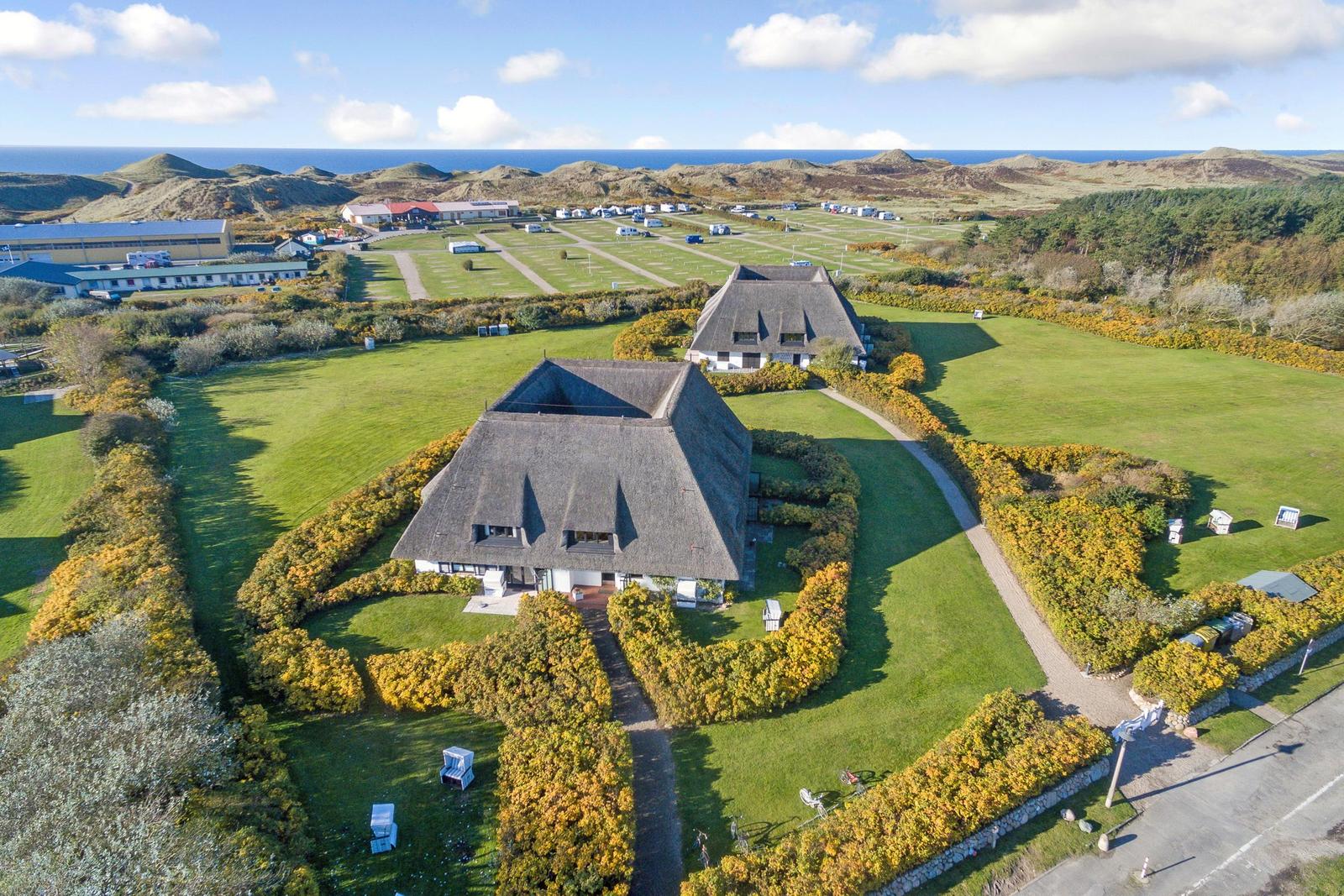 Haus mit strohgedecktem Dach auf grünem Grundstück mit Blick auf Meer und Hügel.