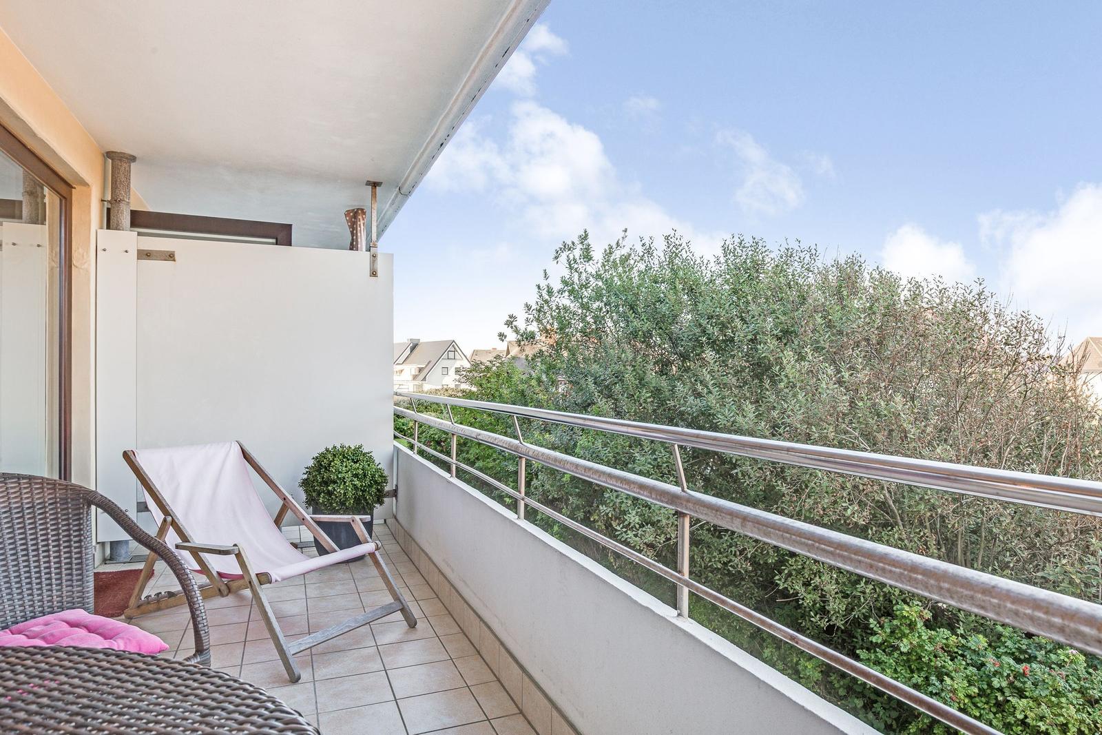 Terrasse mit Liegestuhl und Pflanze. Blick auf grüne Bäume und Himmel.